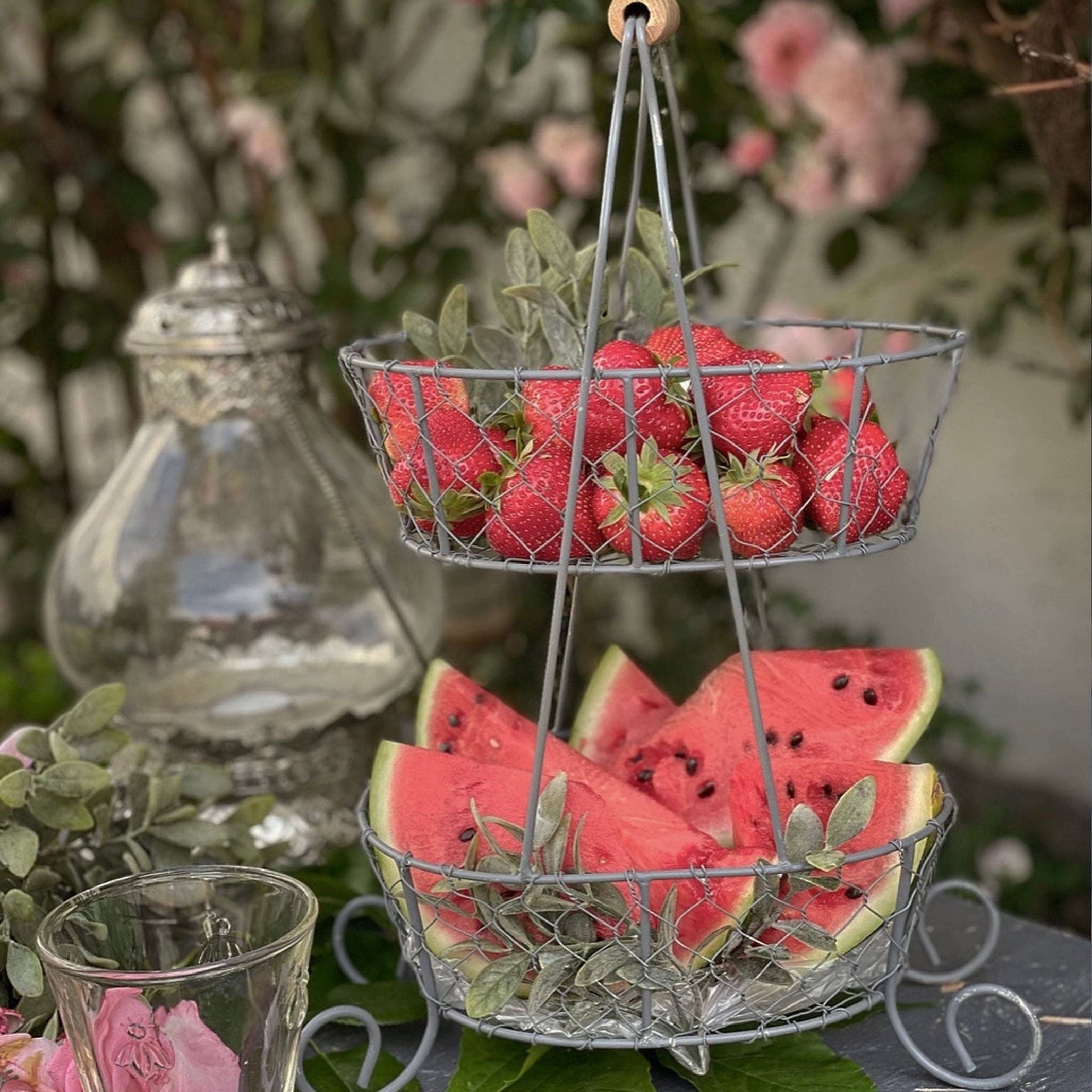 Zweistöckiger Metallkorb mit Erdbeeren und Wassermelonenstücken für den sommerlichen Gartentisch