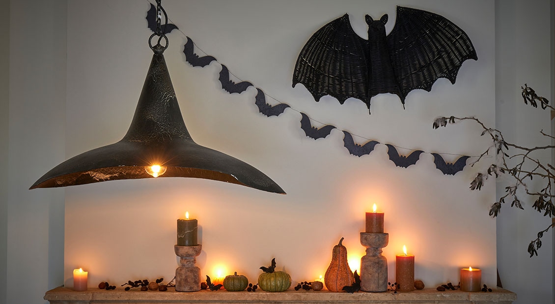 Halloween-Dekoration mit schwarzen Lampen, brennenden Kerzen und Fledermausgirlande an heller Wand