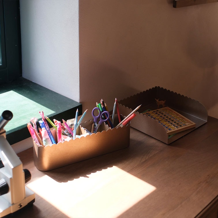 Braune Metall-Organizer mit wellenförmigen Rändern, gefüllt mit Schreibutensilien und einem Buch