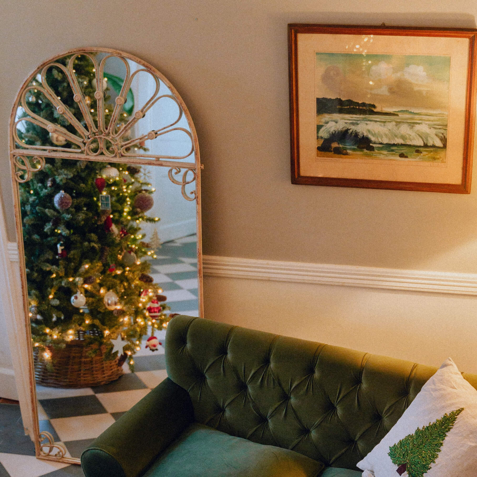 Dekorativer Spiegel mit Metallrahmen, der einen Weihnachtsbaum in einem gemütlichen Wohnzimmer mit grünem Sofa reflektiert.