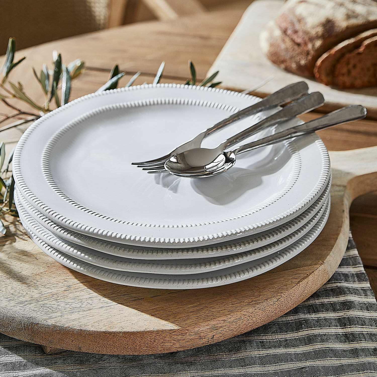 Set aus weissen Keramiktellern mit dekorativem Rand auf einem Holzbrett arrangiert