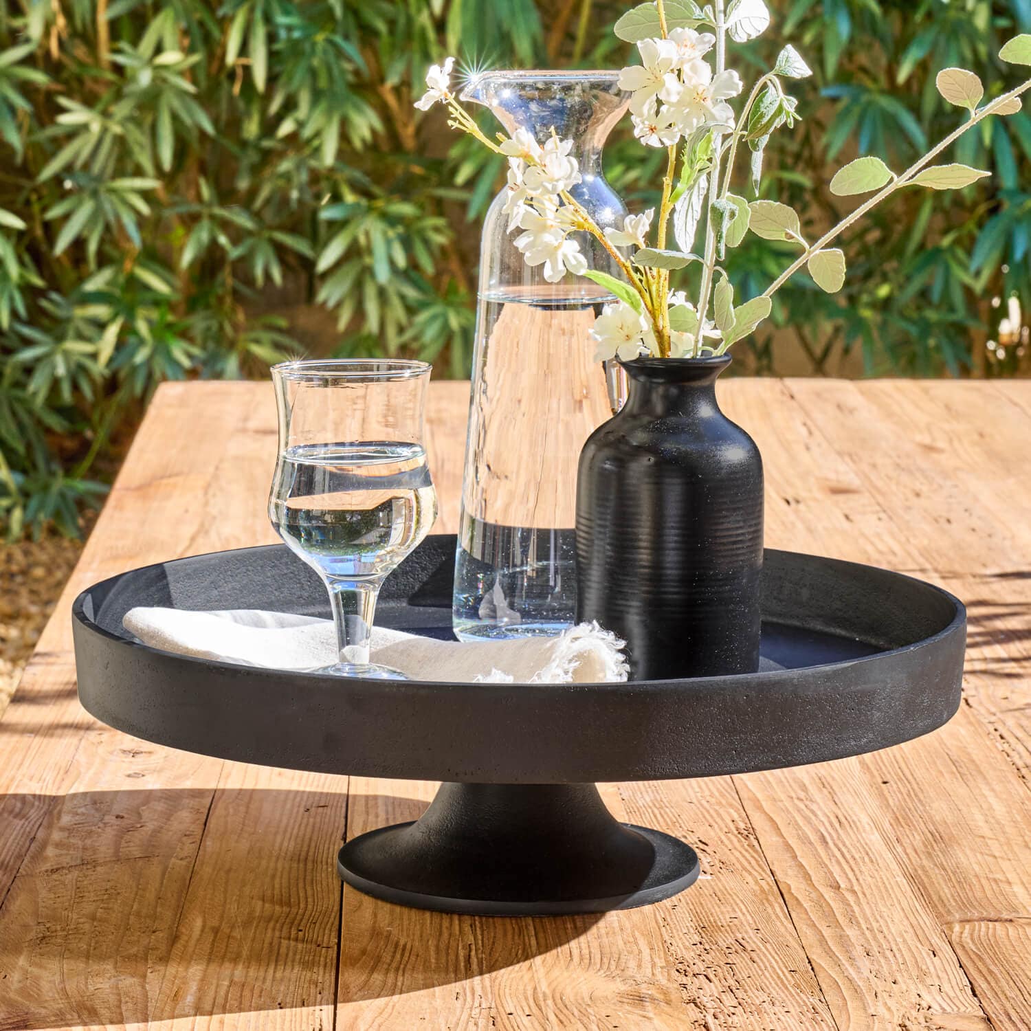 Schwarze Metall-Etagere mit Karaffe, Glas und schwarzer Blumenvase auf hellem Holztisch