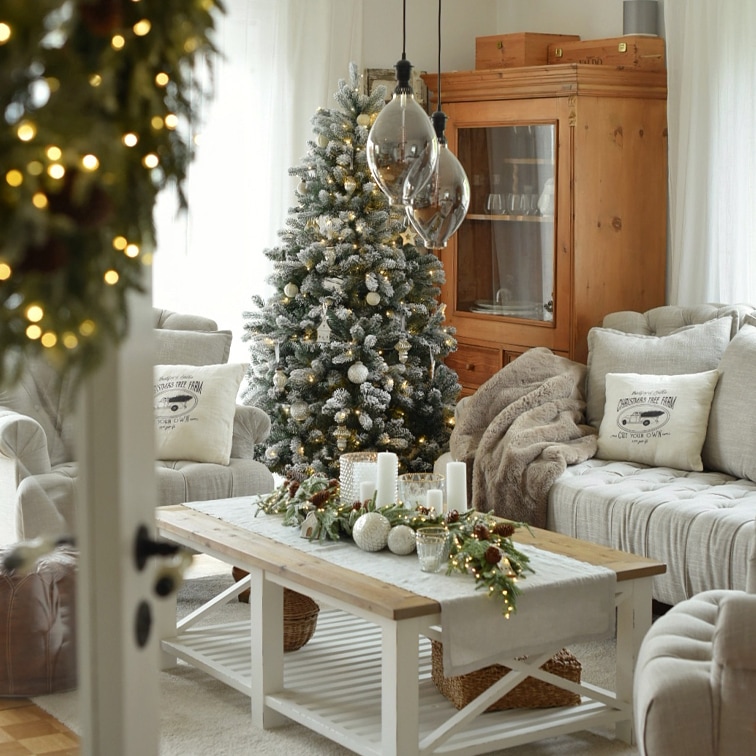 Gemütliches Wohnzimmer mit weissem Holztisch, grauem Sofa und festlich geschmücktem Weihnachtsbaum mit Lichterkette