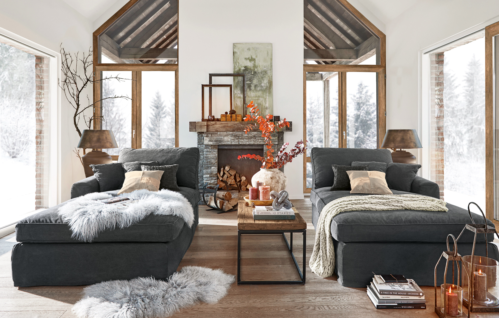 Gemütliches Wohnzimmer im Landhausstil mit zwei dunkelgrauen Sofas und steinernem Cheminée im Hintergrund