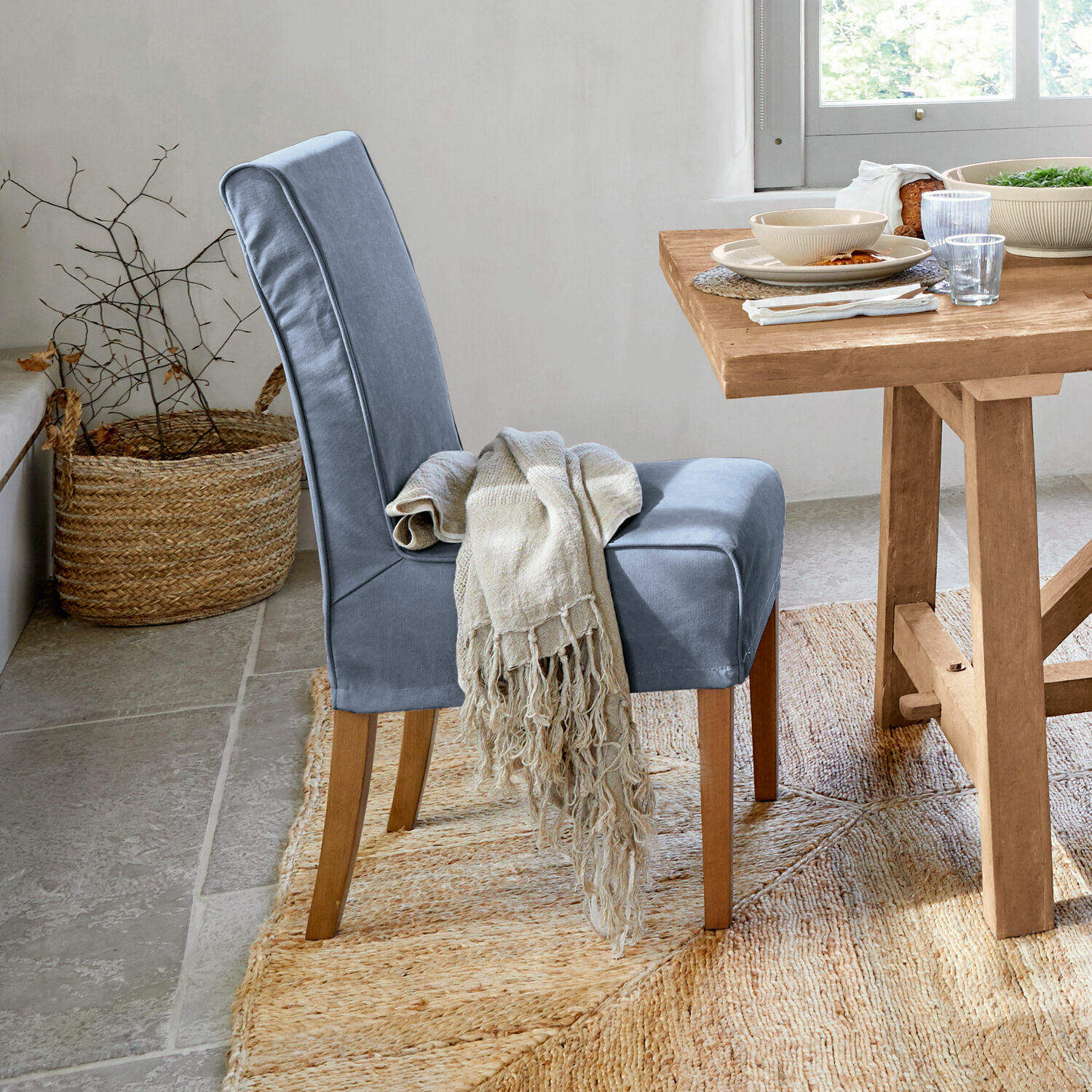 Blau gepolsterter Stuhl mit Holzbeinen und beigem Plaid neben hellem Holztisch.