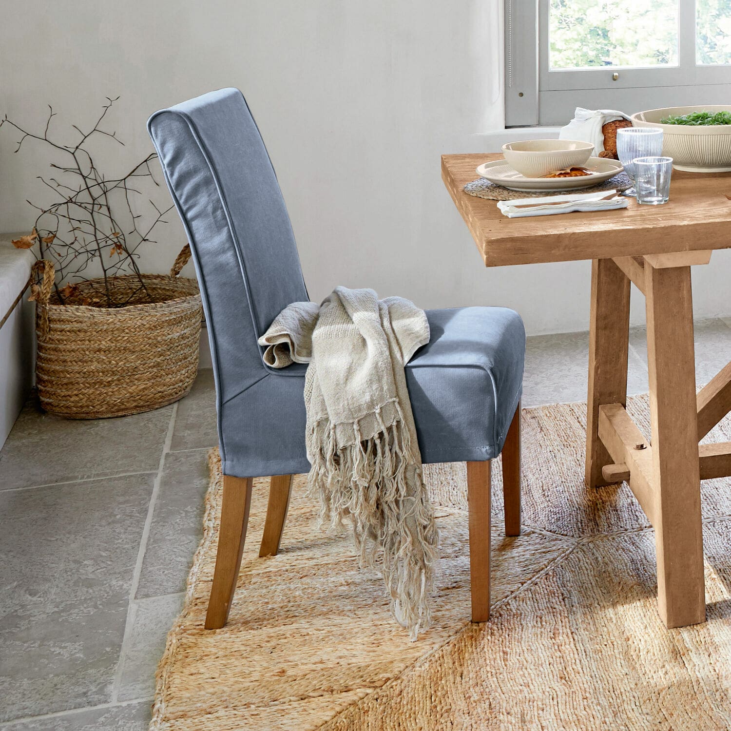Stuhl mit Husse Mankato Blau gepolsterter Stuhl mit Holzbeinen und beigem Plaid neben hellem Holztisch.