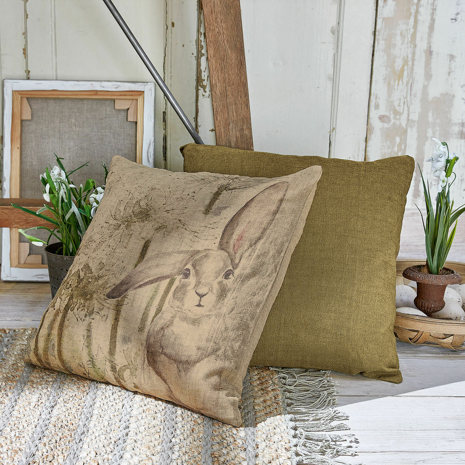 Kissenhülle 2er Set Milda Beiges Kissen mit Hasenmotiv und grünes Dekokissen auf gewebtem Teppich