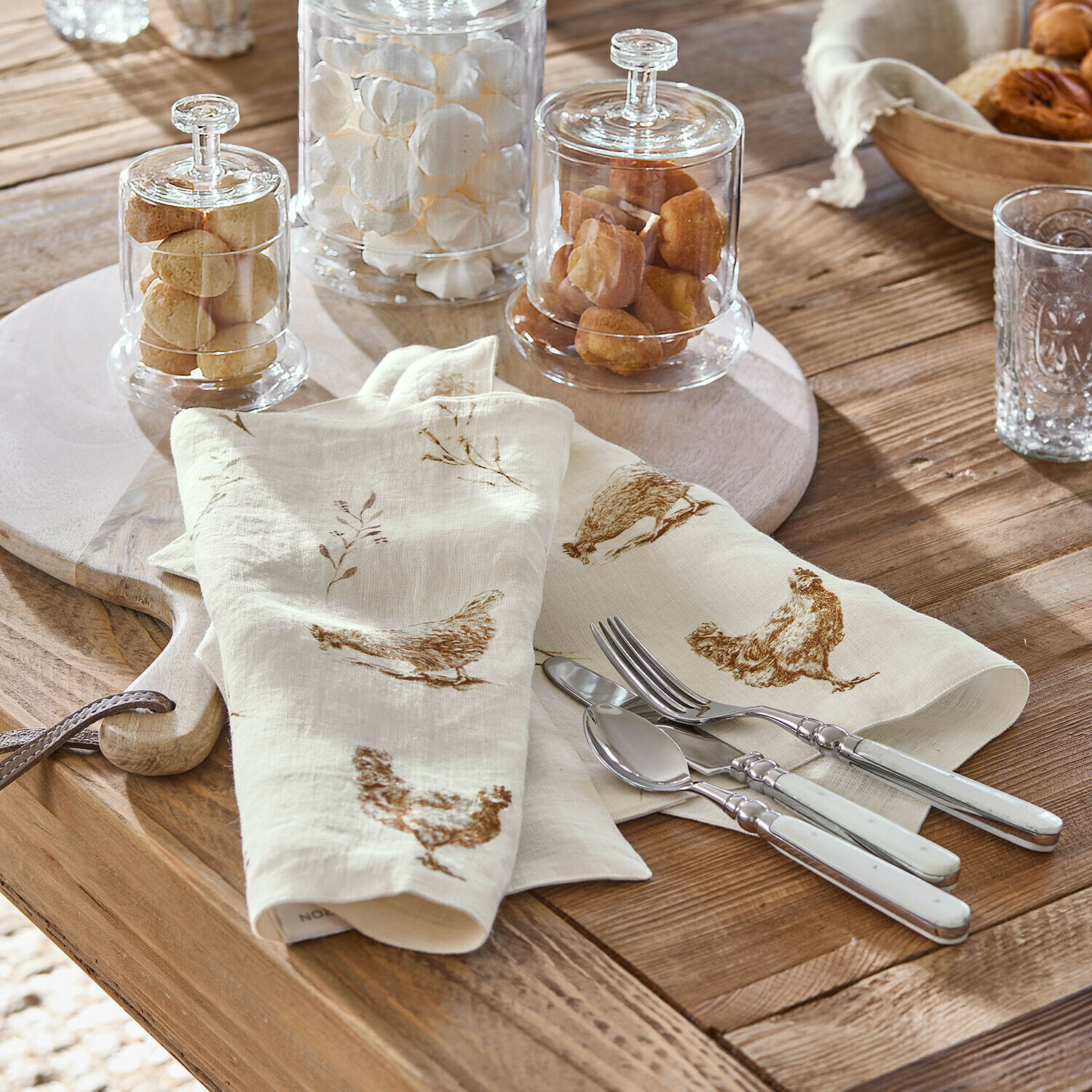 Platzset 2er Set Chavéreau Leinenservietten in Creme mit braunem Hühnermotiv auf Holztisch mit Metallbesteck