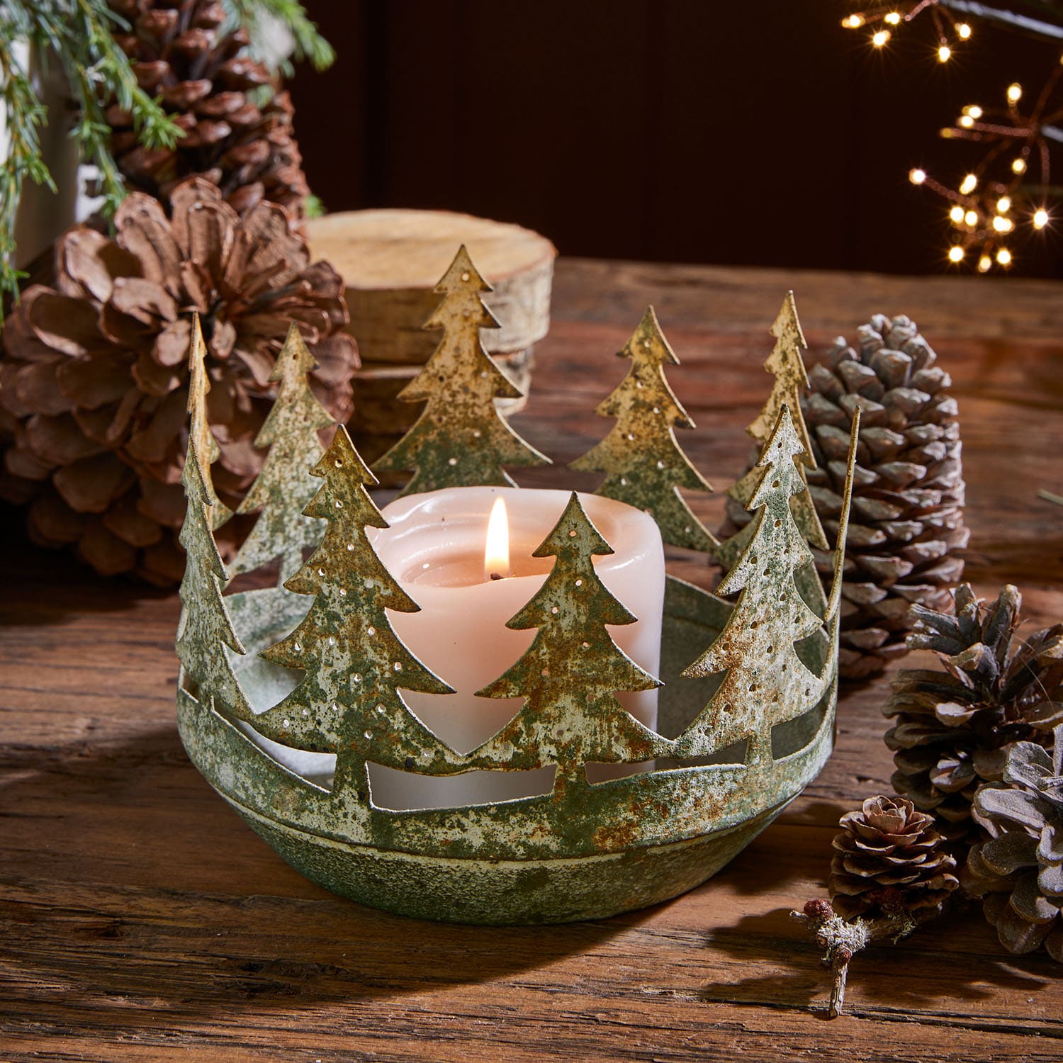 Metall-Kerzenhalter mit Tannenbaum-Motiv in grün-roster Optik und weisser Kerze auf Holztisch