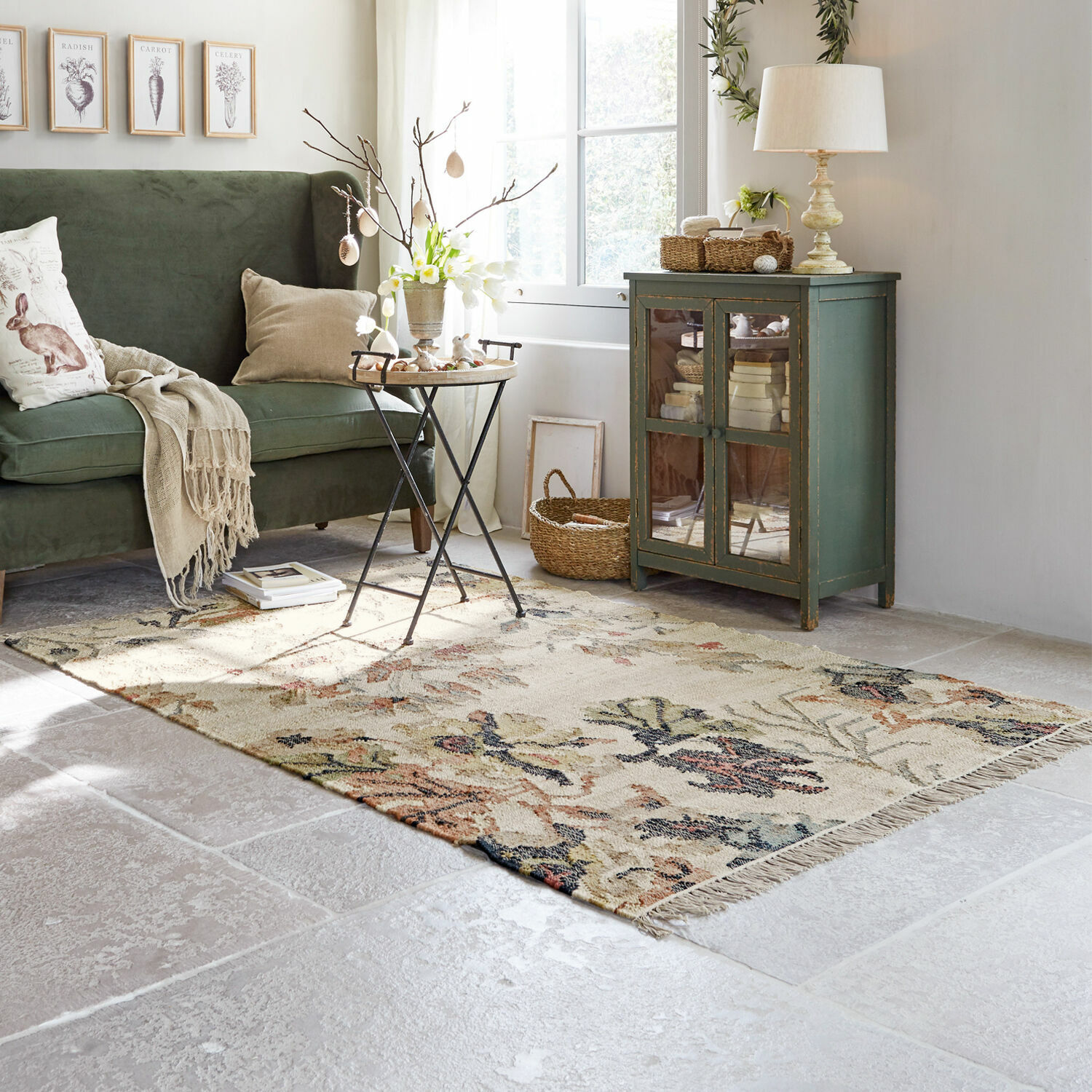 Gemütliches Wohnzimmer mit grünem Sofa, Holzschrank und floralem Teppich auf hellem Boden