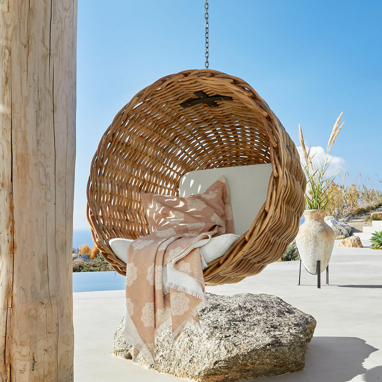 Hängesessel Nirevox Hängesessel aus natürlichem Rattan mit hellem Kissen und rosa Decke auf der Terrasse mit Meerblick
