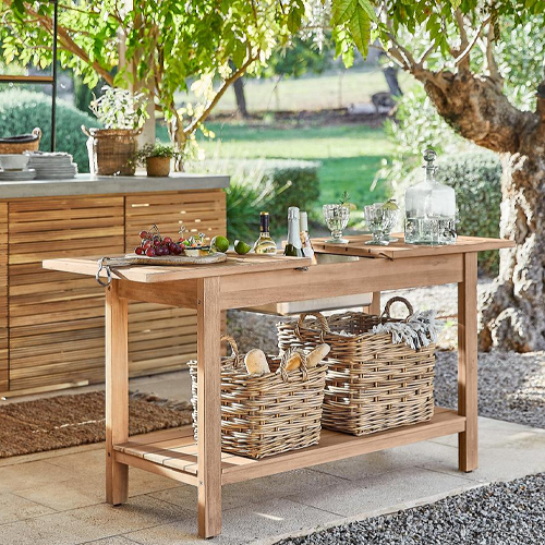 Gartentisch aus Naturholz mit geflochtenen Körben und Servierutensilien auf der sonnigen Terrasse