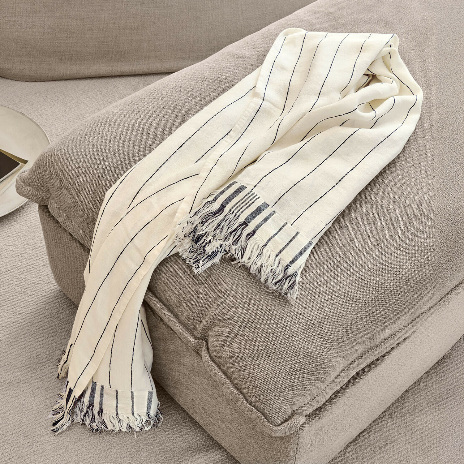 Plaid Ulderina Beige Baumwoll-Decke mit schwarzen Streifen und Fransen auf grauem Sessel, gemütliche Wohnraumdeko