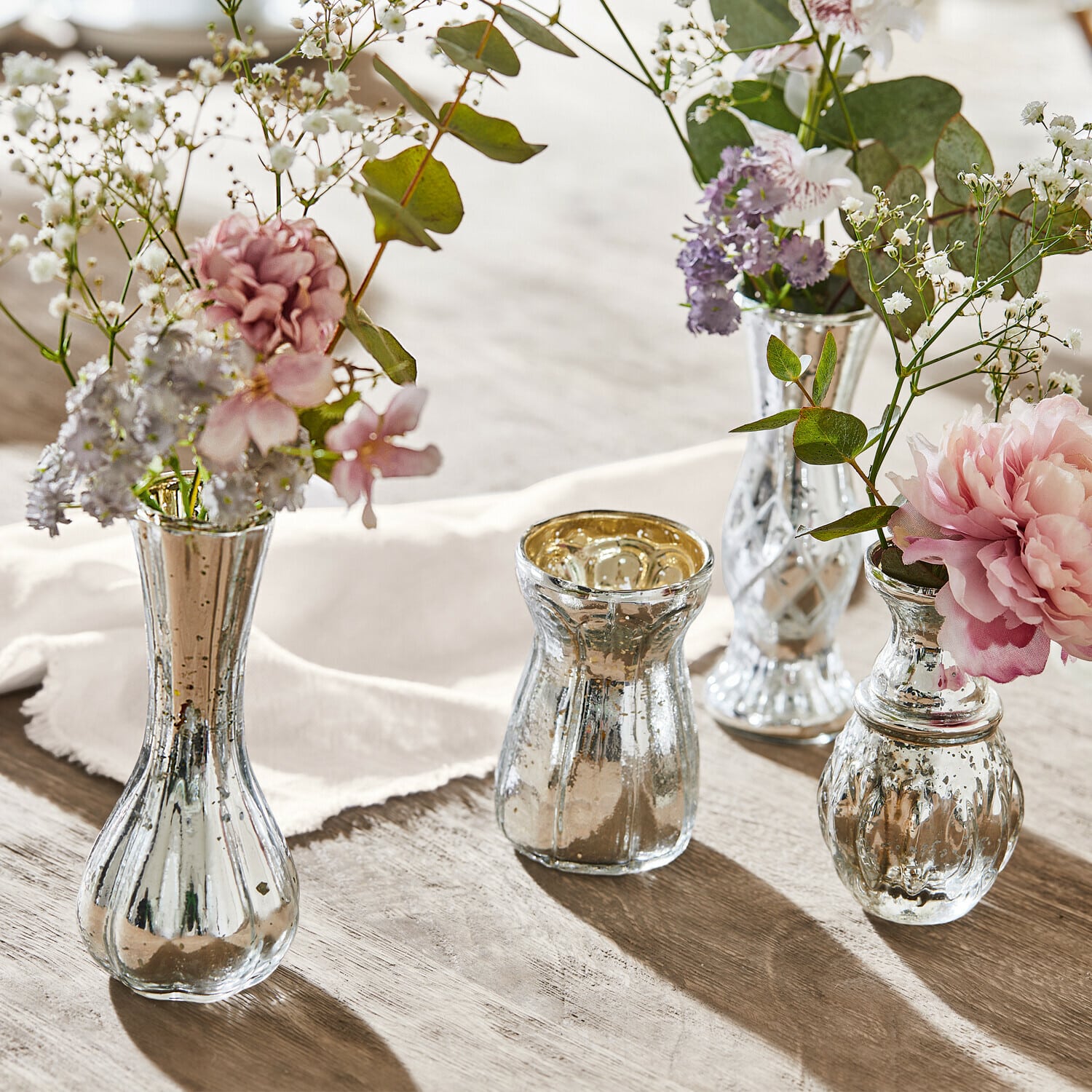 Deko-Vase 4er Set Maelie Vier silberne Glasvasen mit Blumen auf einem Holztisch, stilvolle Tischdekoration im Vintage-Stil
