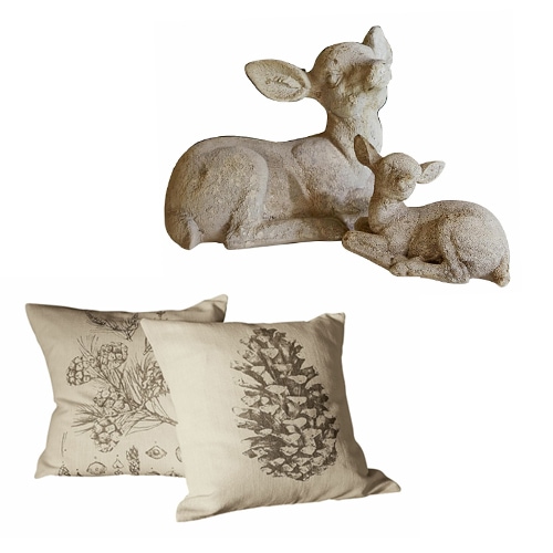 Dekoration mit zwei beigen Kissen mit Zapfen- und Blumenmotiv sowie einer Steinfigur von zwei Rehen