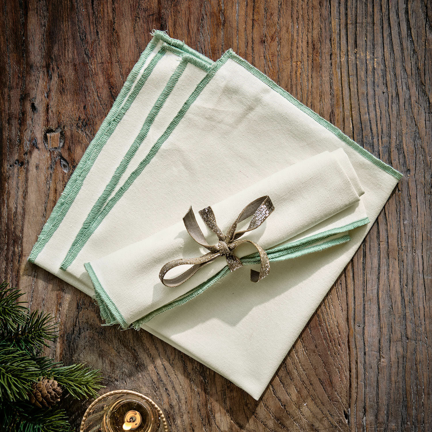 Serviette 2er Set Tarivelle Set aus cremefarbenen Leinenservietten mit grünem Rand auf Holztisch, festliche Dekoration