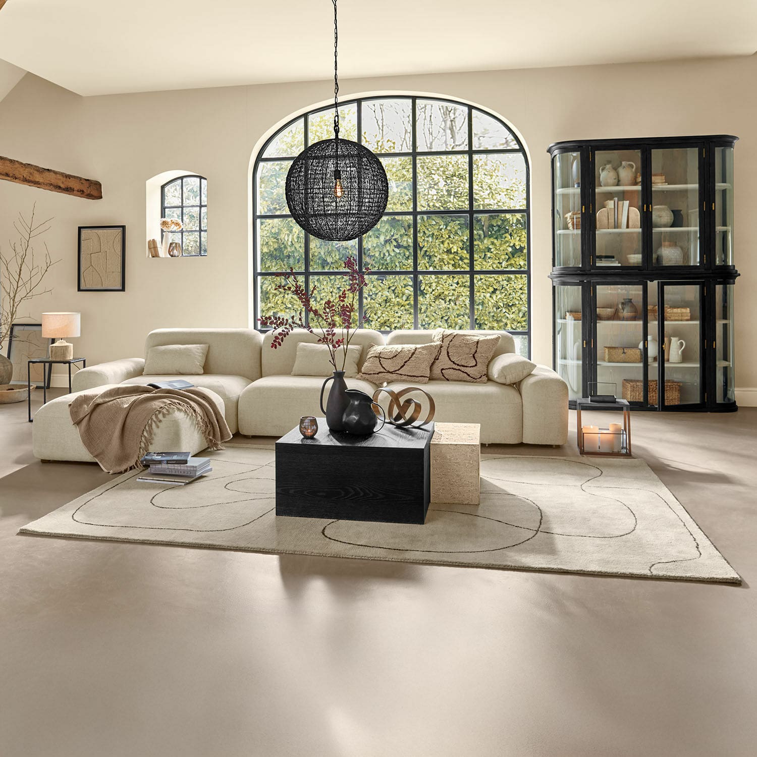 Geräumiges Wohnzimmer mit beigem Stoffsofa und schwarzem Holztisch auf gemustertem Teppichboden