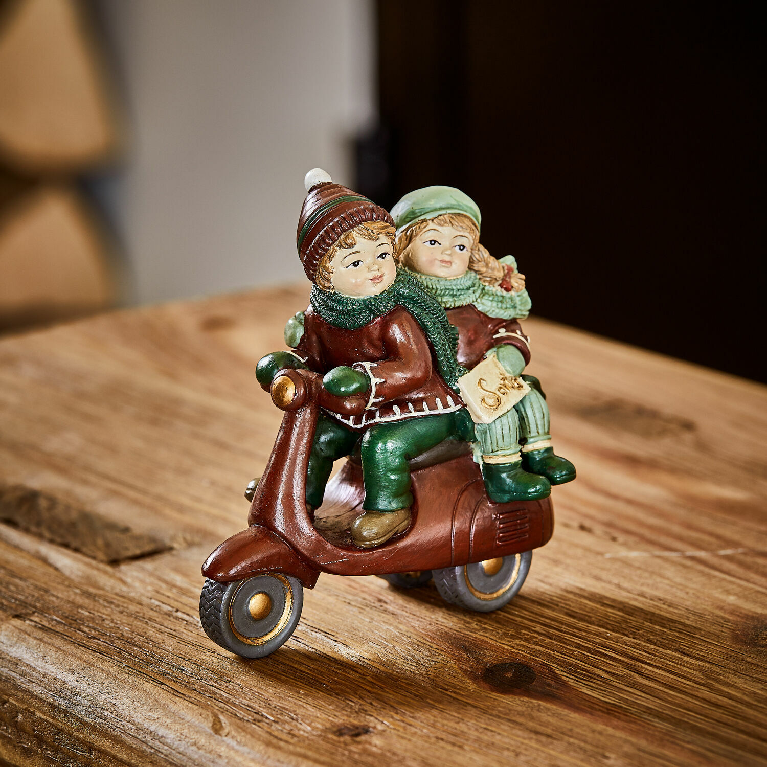 Deko-Figur Dariell Figur mit zwei Kindern auf braunem Roller in grüner Kleidung auf Holztisch als Winterdekoration