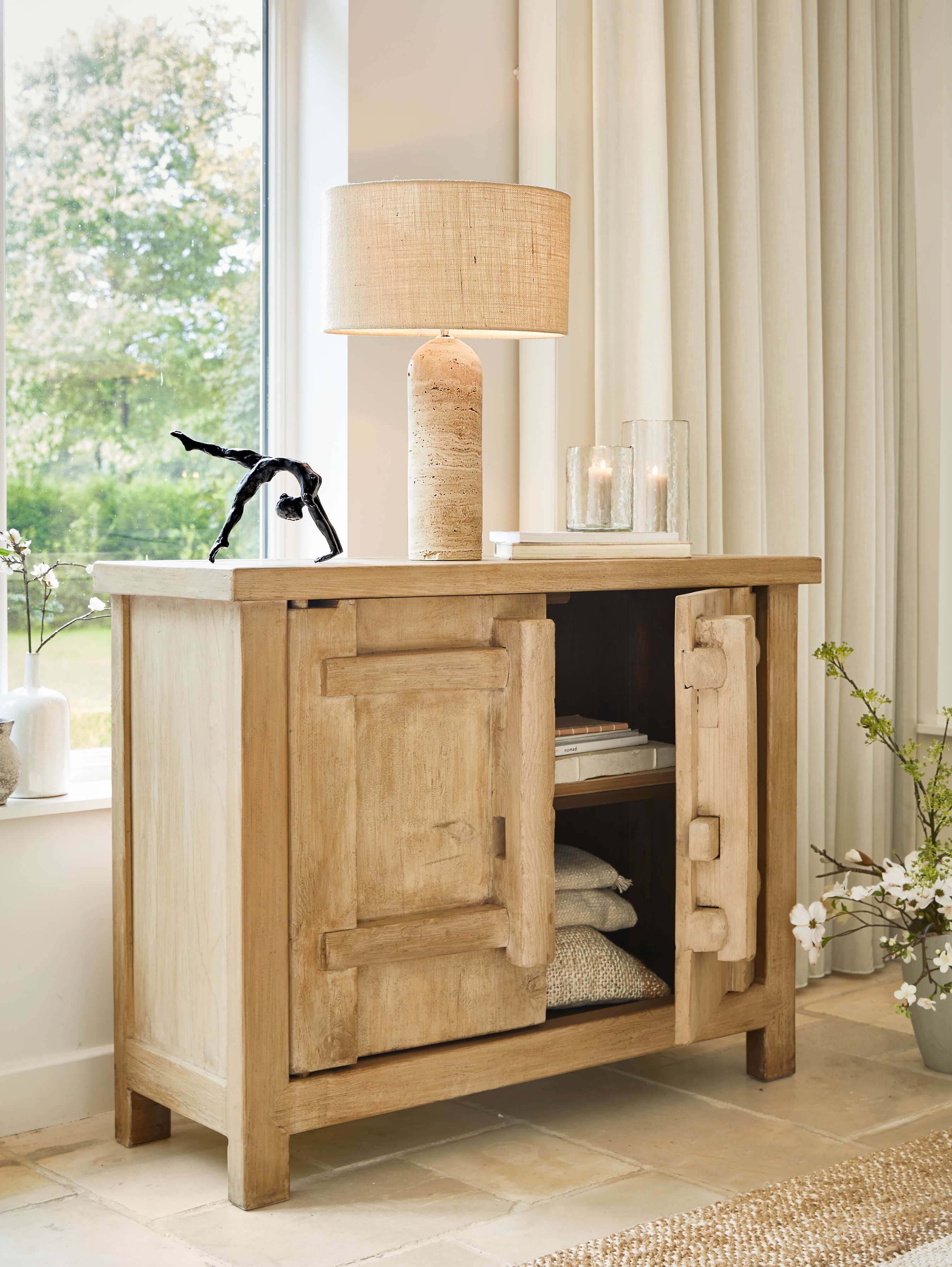 Helle Holzkommode mit offenen Türen, beiger Lampe und Dekoration im hellen Wohnzimmer