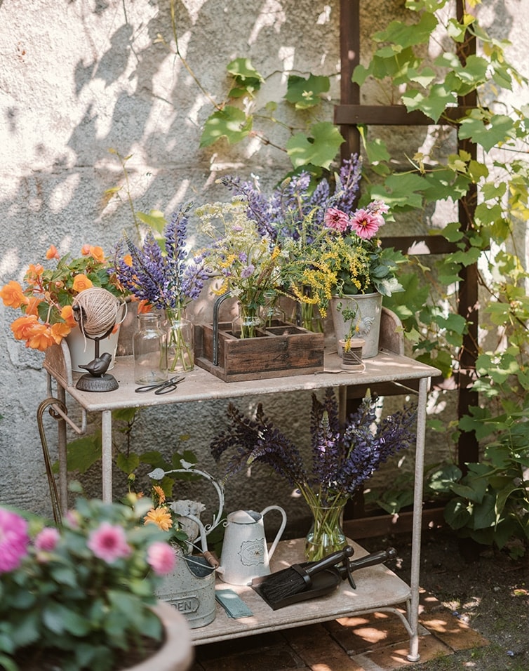 Metall-Gartentisch mit Blumen und Gartengeräten an einem sonnigen, schattigen Ort
