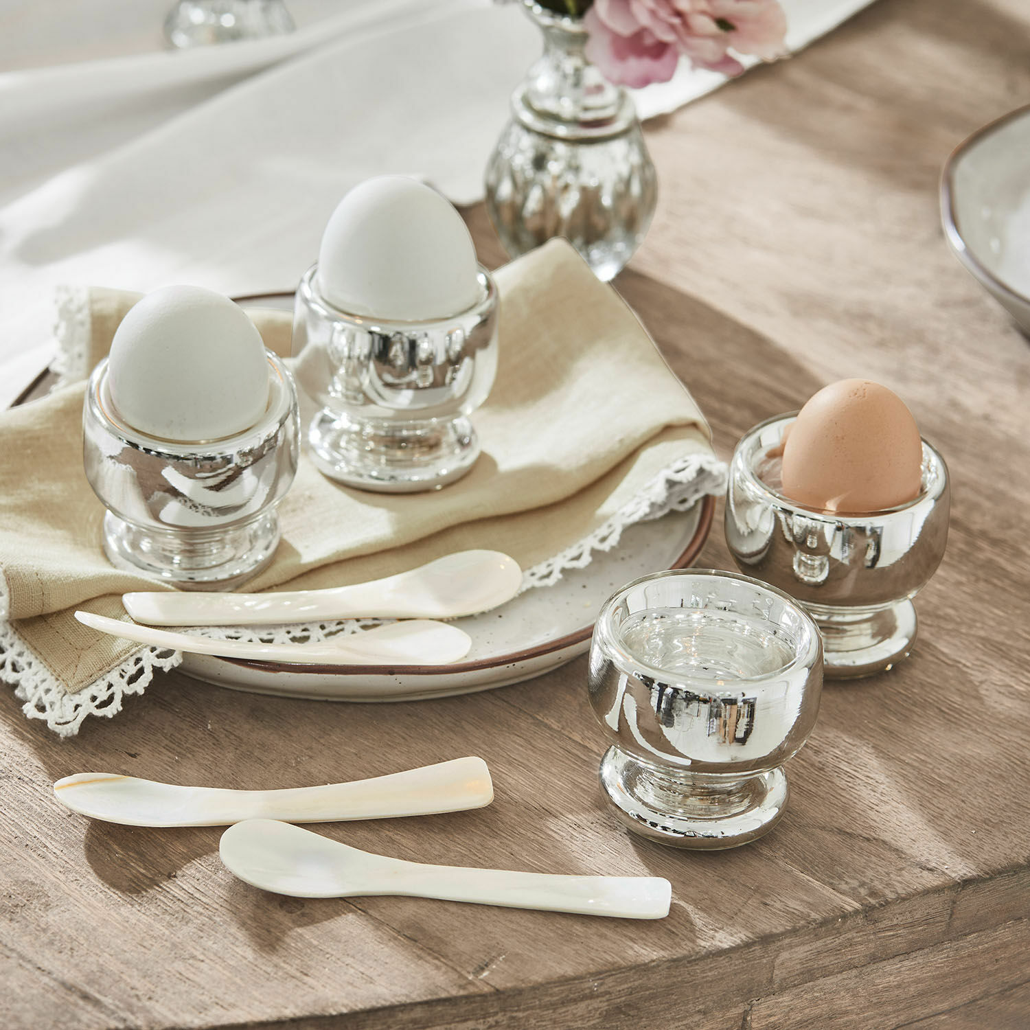 Eierbecher 4er Set Lilligret Set aus silbernen Metall-Eierbechern mit weissen und braunen Eiern und weissen Löffeln auf Holztisch