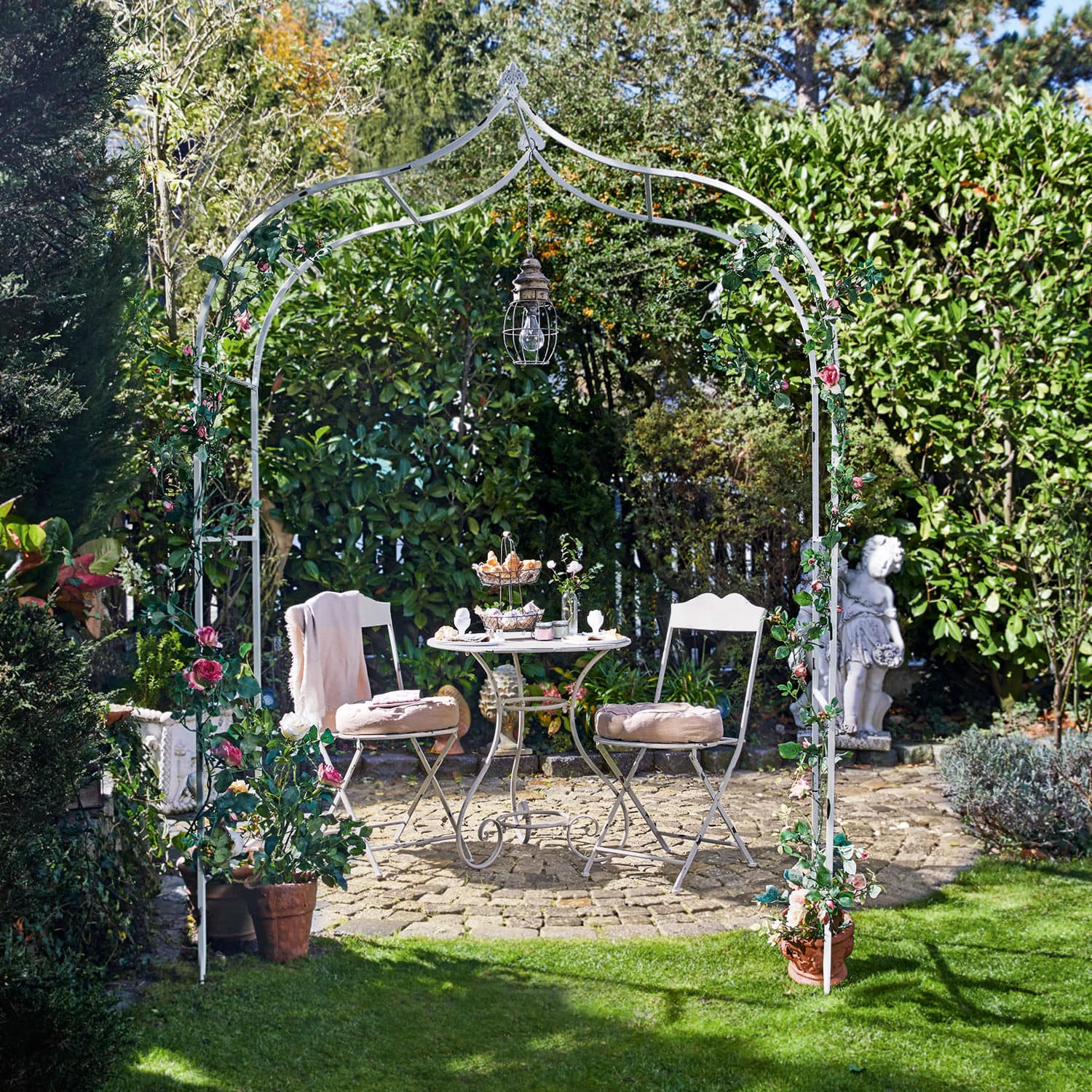 Rosenbogen Dimarus Weisser Metall-Gartenbogen mit rosa Blumen und Hängelampe, davor Sitzgruppe auf Steinpflasterung