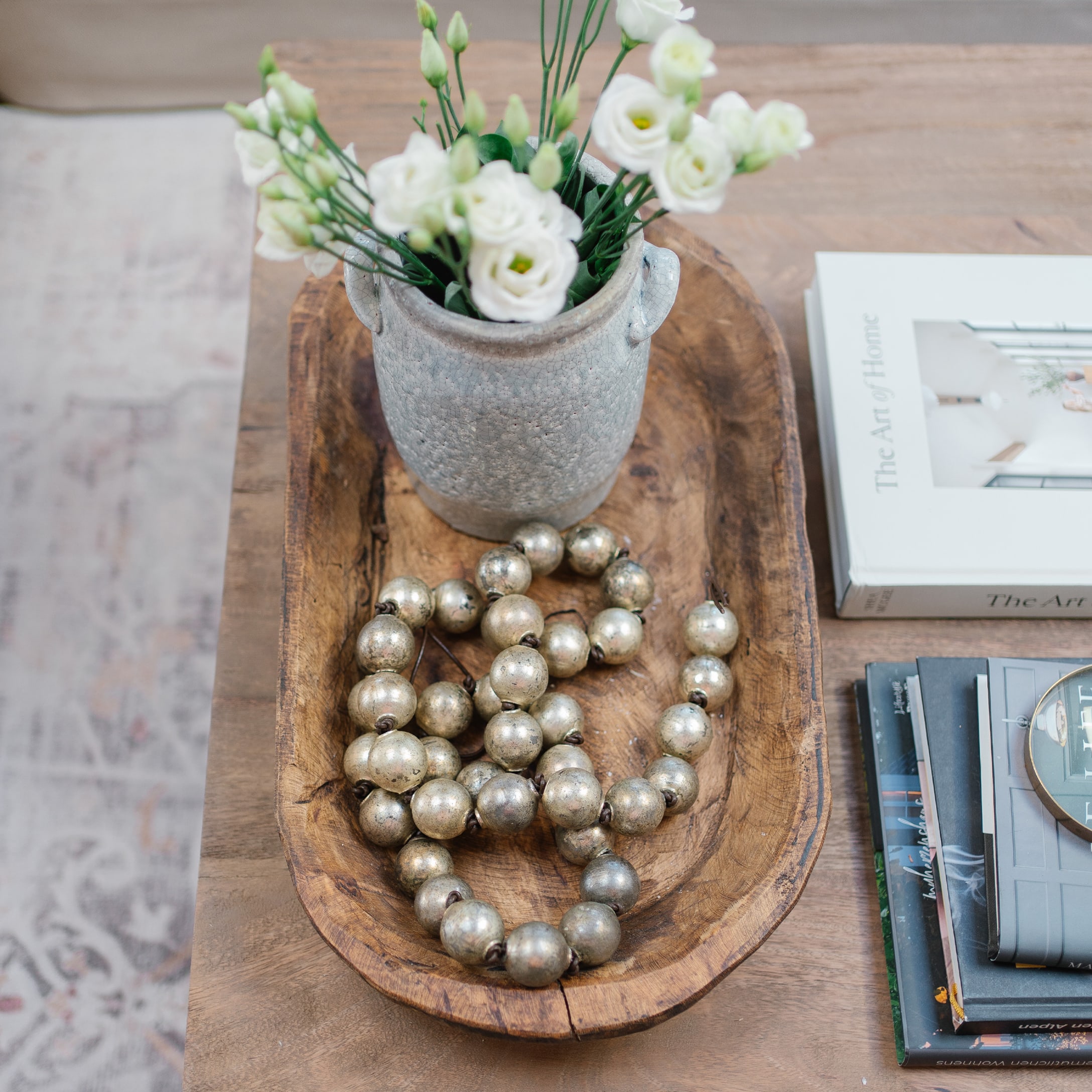 Holzschale mit grauer Keramikvase, weissen Blumen und dekorativer Metallperlenkette auf Holztisch