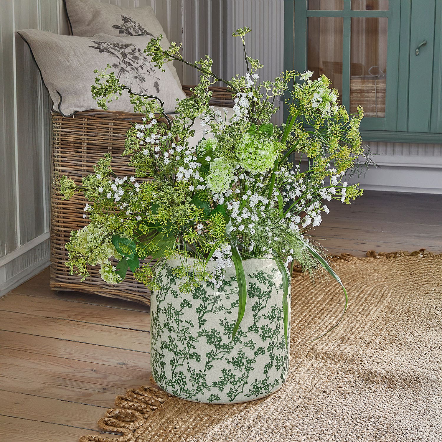 Keramikvase mit grünem Muster und weißen sowie grünen Blumen auf hellem Holzboden