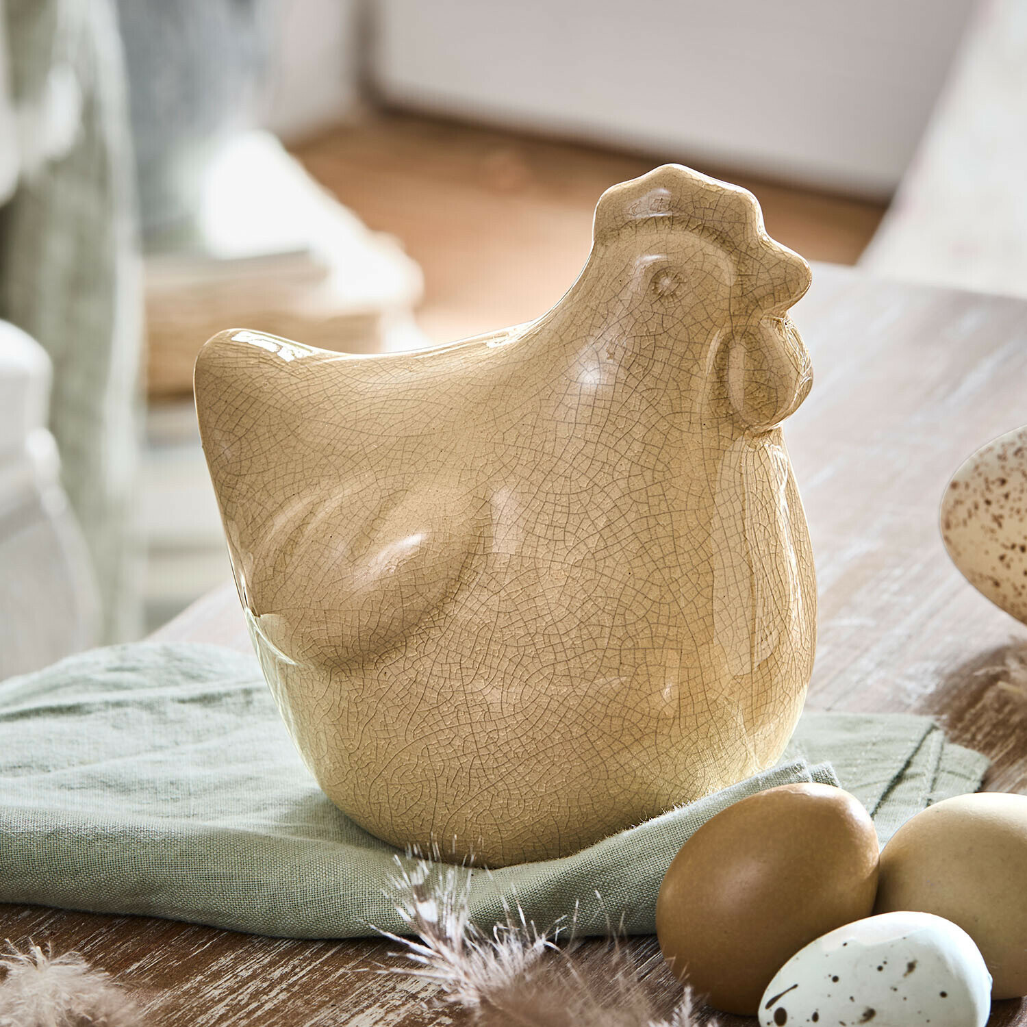 Deko-Huhn Roisenn Beige Keramik-Hühnerfigur mit Craquelé-Effekt auf grünem Stoff neben dekorativen Eiern