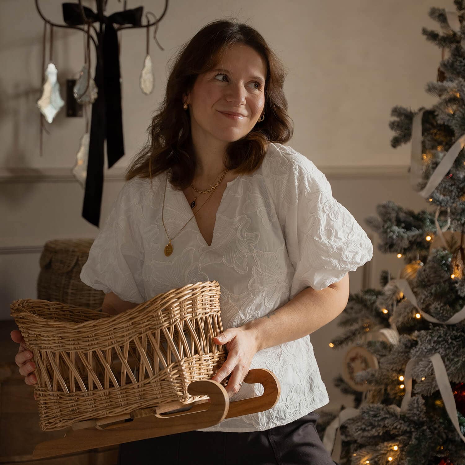 Frau in weisser Bluse hält einen Korbschlitten aus Weide mit Holzgestell neben geschmücktem Weihnachtsbaum