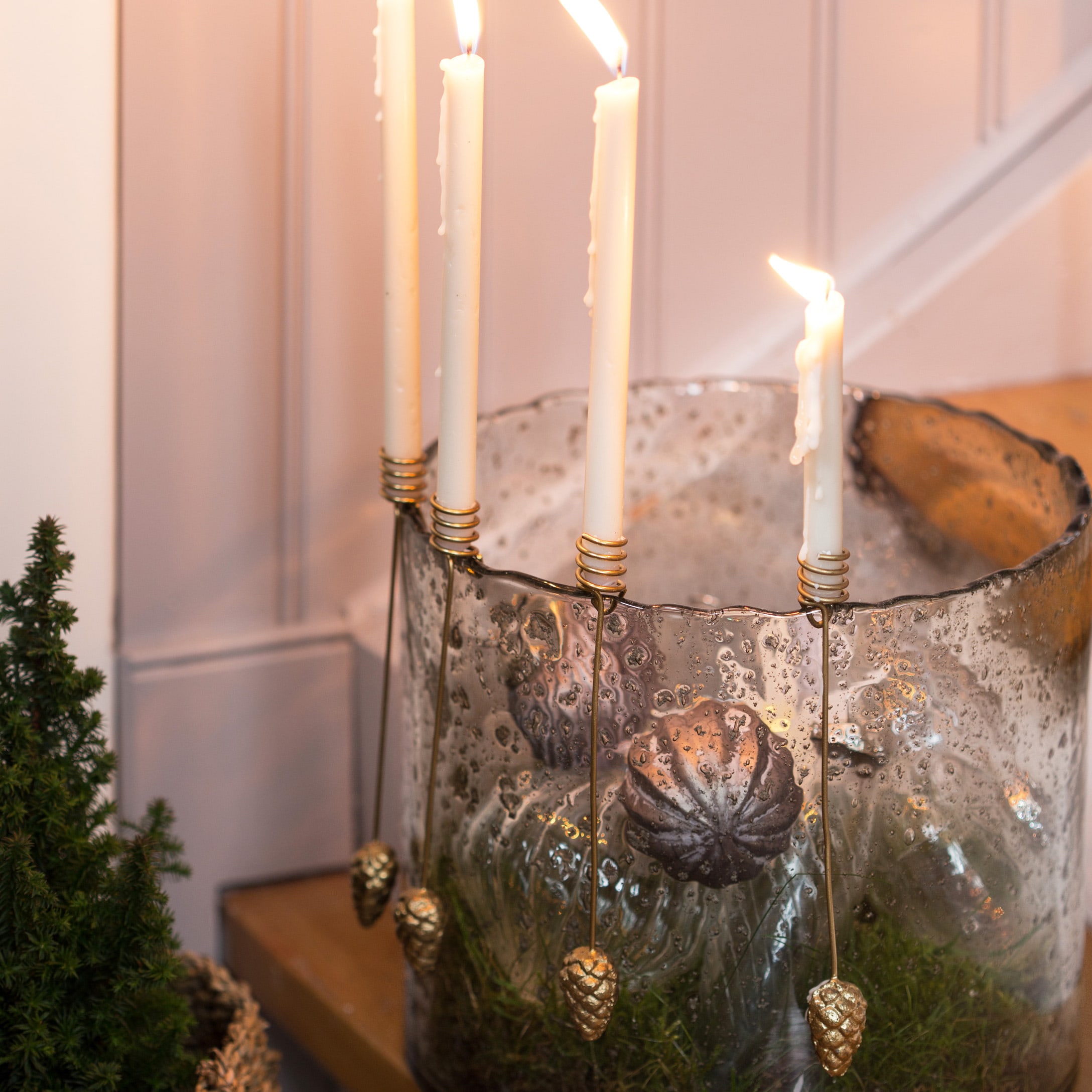 Glaskerzenhalter mit weissen Kerzen und goldenen Zapfenanhängern auf Holztisch dekoriert
