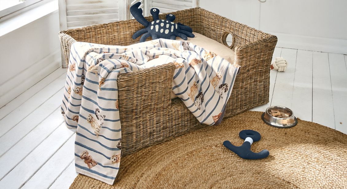 Wickelkorb-Hundebett mit beigem Kissen und gestreifter Decke mit Hundemotiven, maritime Spielzeuge