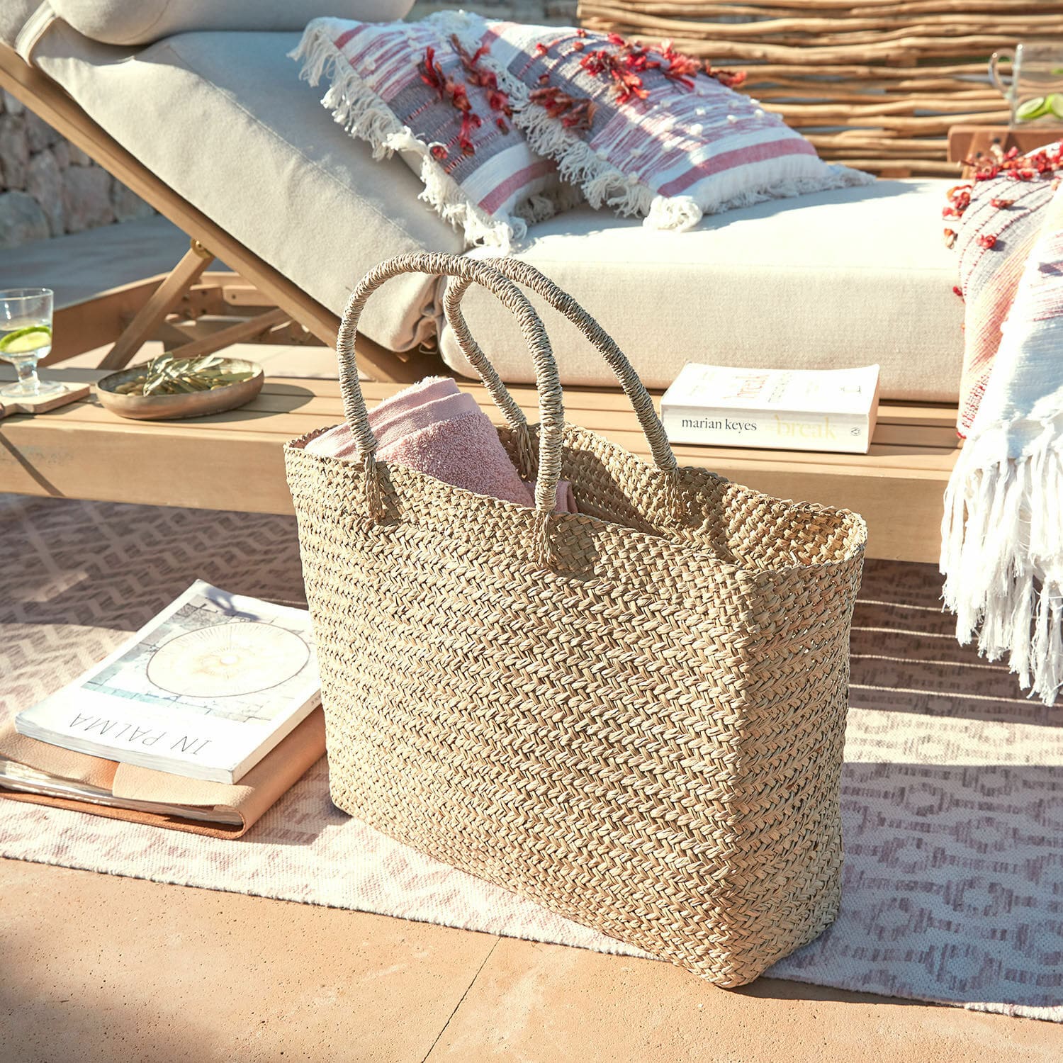Tasche Ventresque Natürliche, geflochtene Tasche aus Seegras mit rosa Handtuch auf der Terrasse neben dem Liegestuhl
