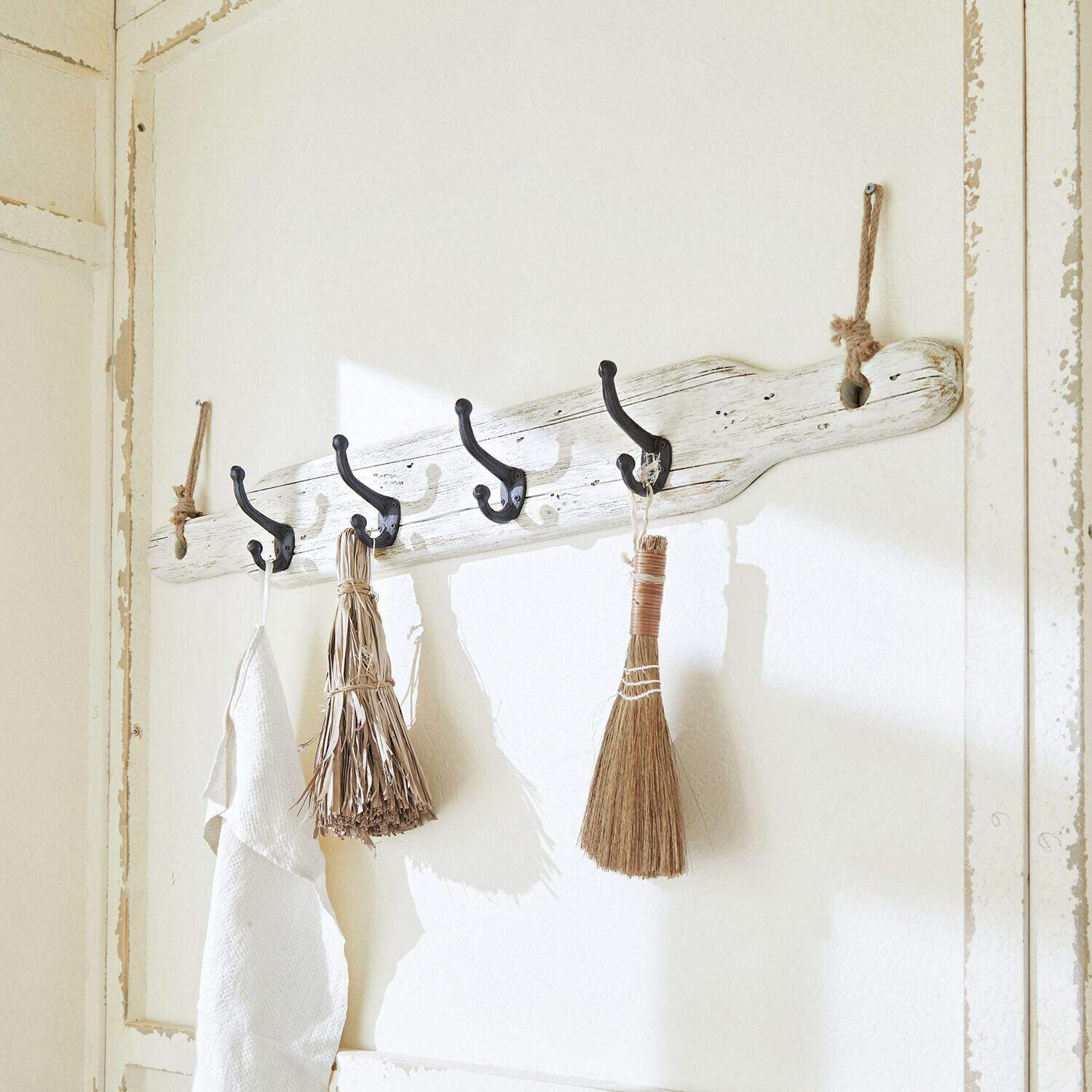 Rustikaler Wandhaken aus weiss lackiertem Holz mit schwarzen Haken und natürlichen Dekobesen
