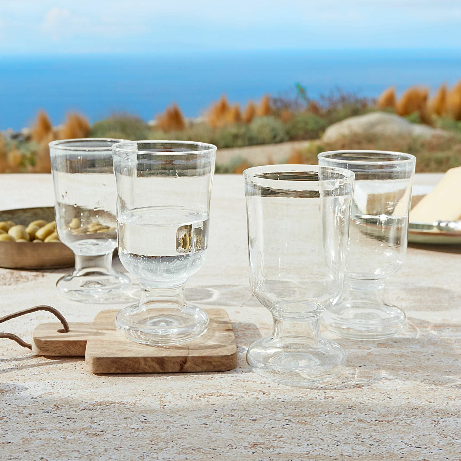 Glas 4er Set Yvoncourt Vier transparente Gläser mit Stiel auf dem Tisch mit Meerblick, modernes Trinkgeschirr