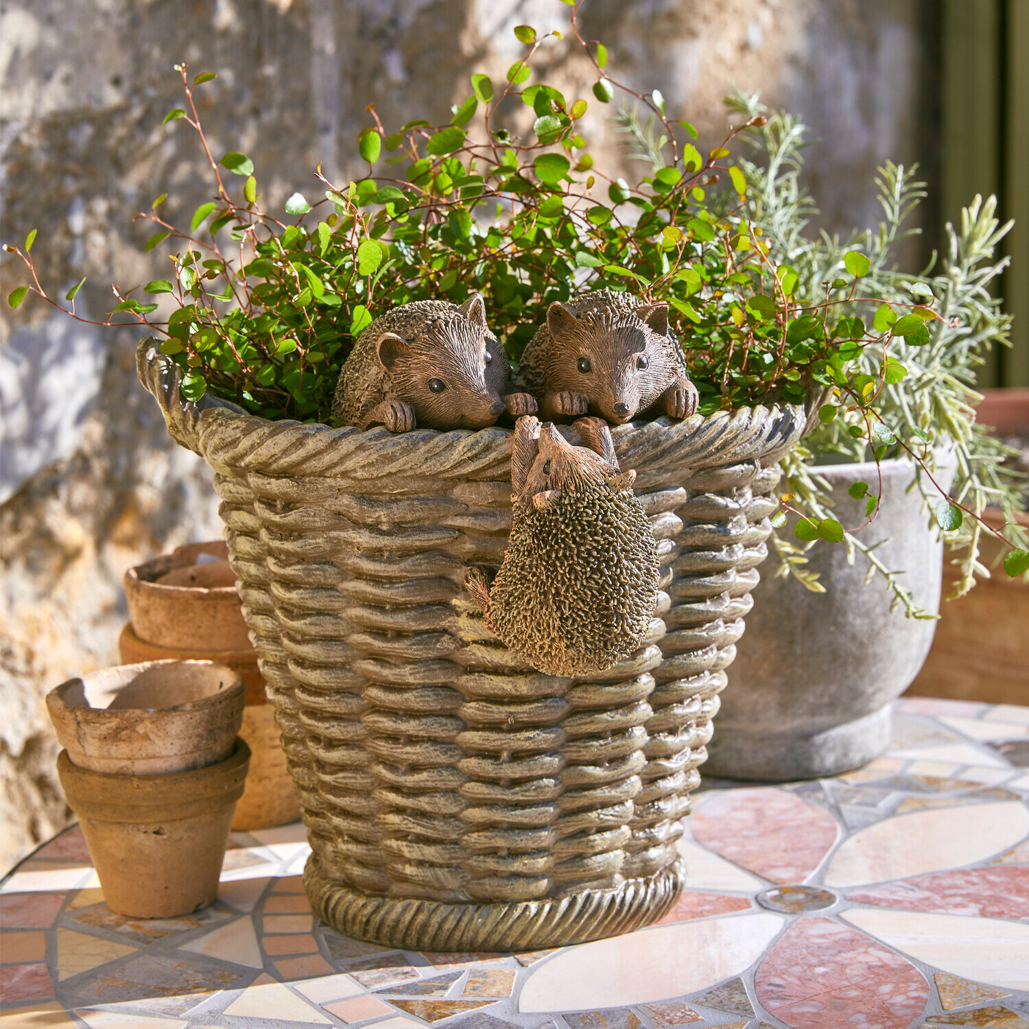 Grauer Kunststoff-Blumentopf mit Igel-Dekor und grünen Pflanzen auf Mosaik-Terrasse