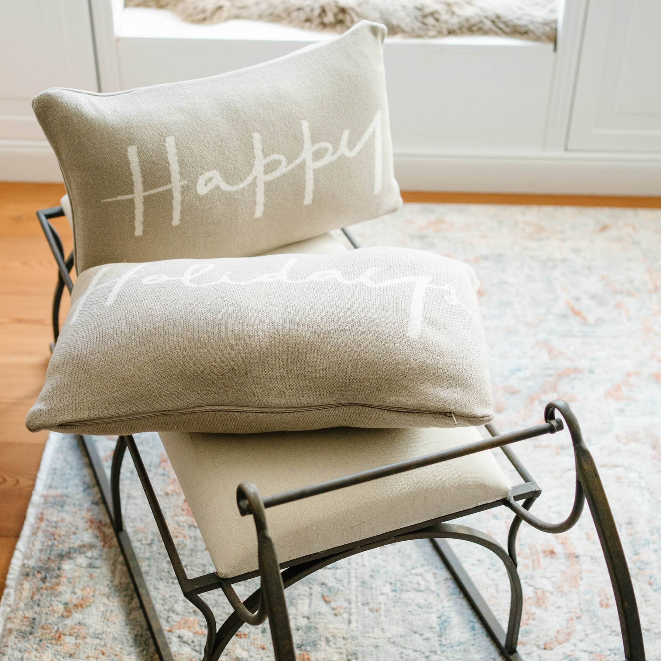 Beige Kissen mit Aufschrift „Happy Holidays“ auf Metallrahmen auf Teppich in hellem Raum