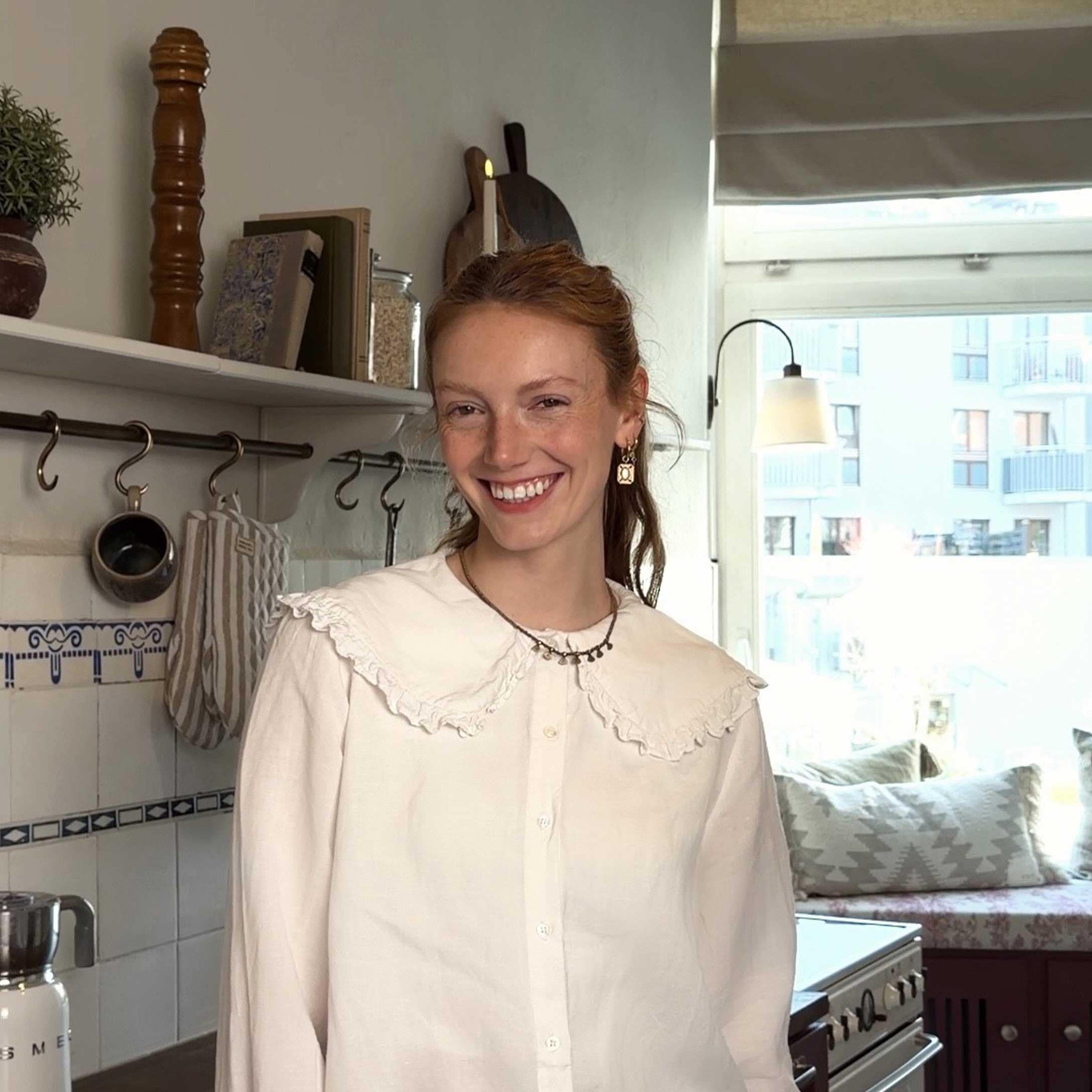Frau in weisser Bluse mit Rüschen in heller Küche mit dekorativen Accessoires und Fenster