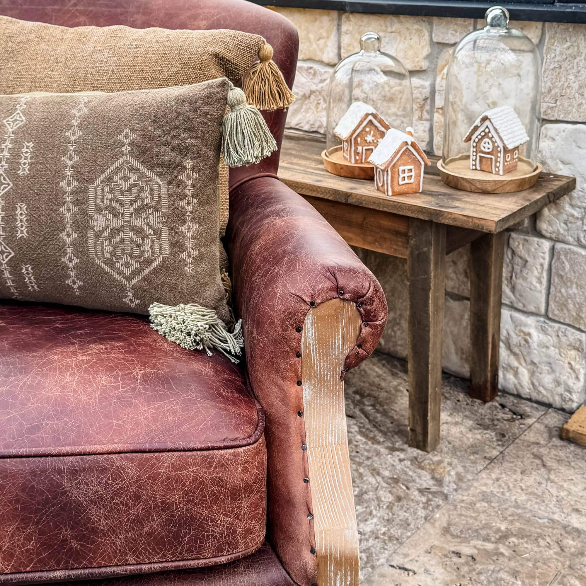 Braunes Ledersofa mit dekorativen Kissen und Holztisch mit Lebkuchenhäusern unter Glaskuppeln.