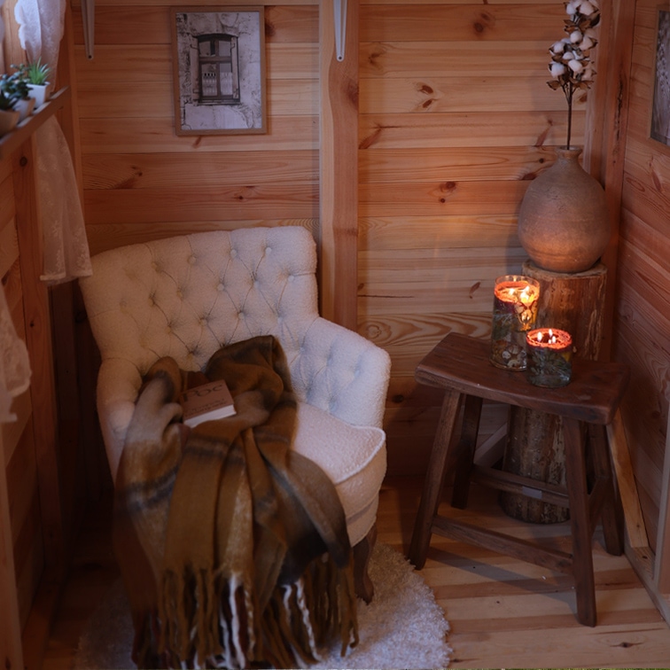 Gemütliche Ecke mit weissem, gepolstertem Sessel, braunem Plaid und Holzschemel mit brennenden Kerzen