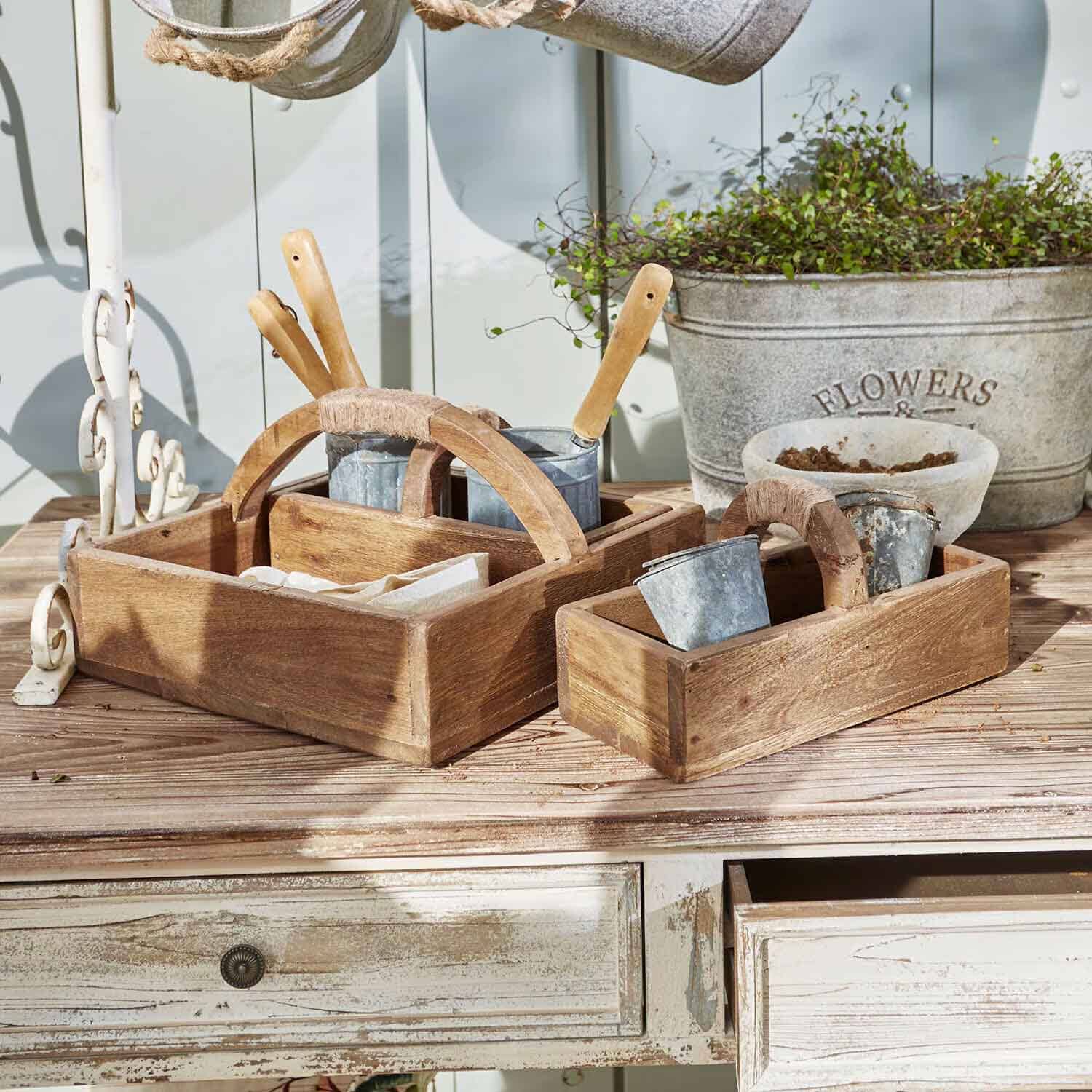 Holzkisten mit Griffen, Gartengeräte und Metalltöpfe auf einem Holztisch arrangiert