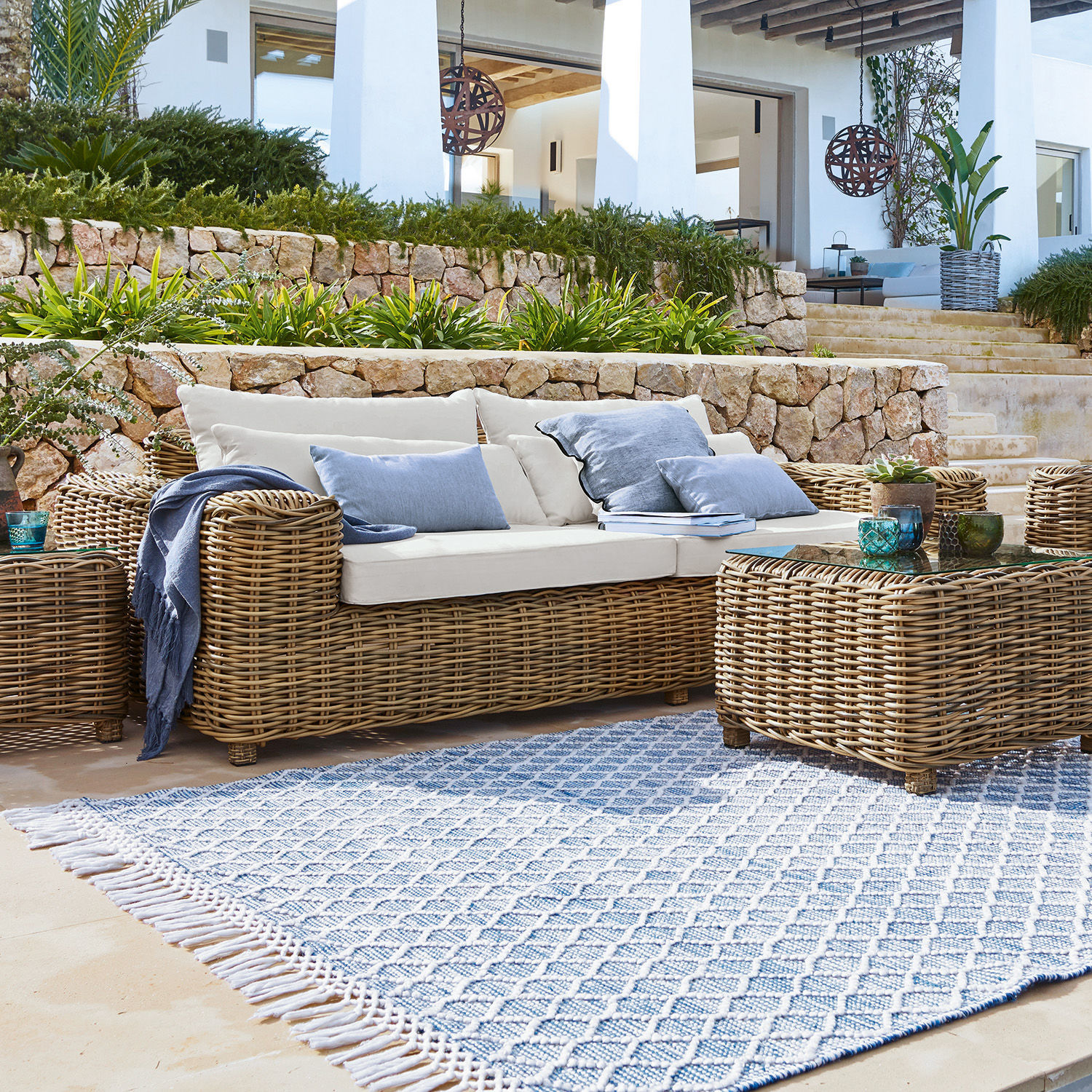 Sofa Camas Gartenmöbel-Set aus natürlichem Rattan mit cremefarbenen Kissen und blau gemustertem Teppich