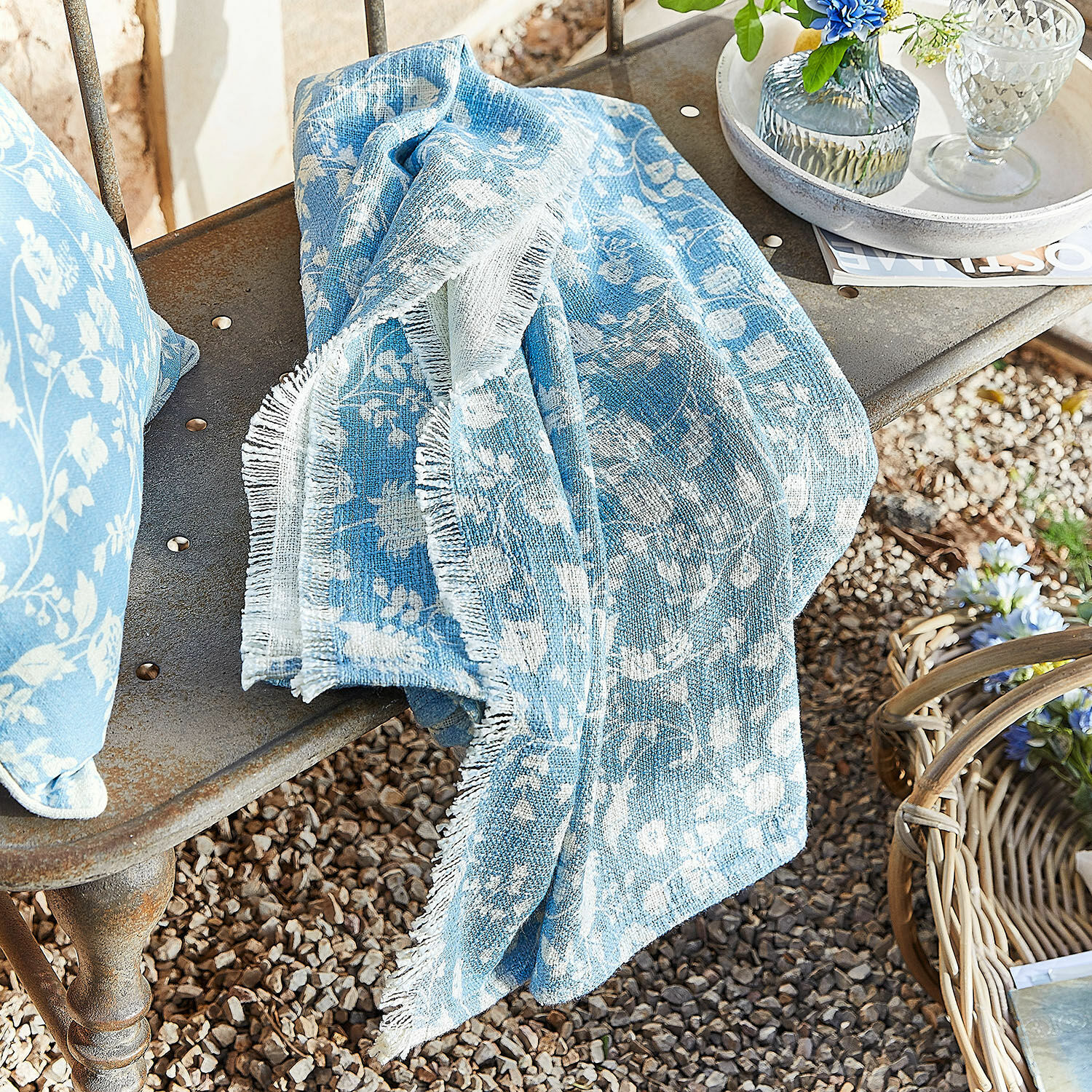 Plaid Corvelique Blaues Baumwollplaid mit weissem Blumenmuster auf Metallbank im Garten drapiert