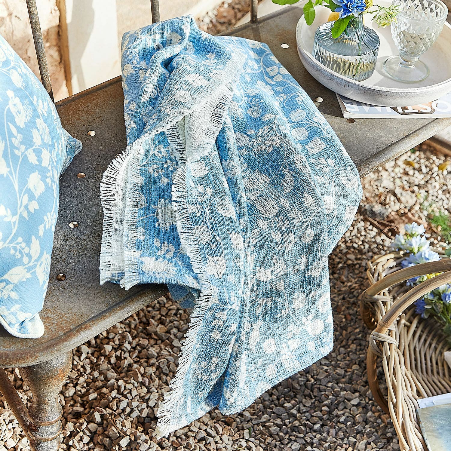 Plaid Corvelique Blaues Baumwollplaid mit weissem Blumenmuster auf Metallbank im Garten drapiert