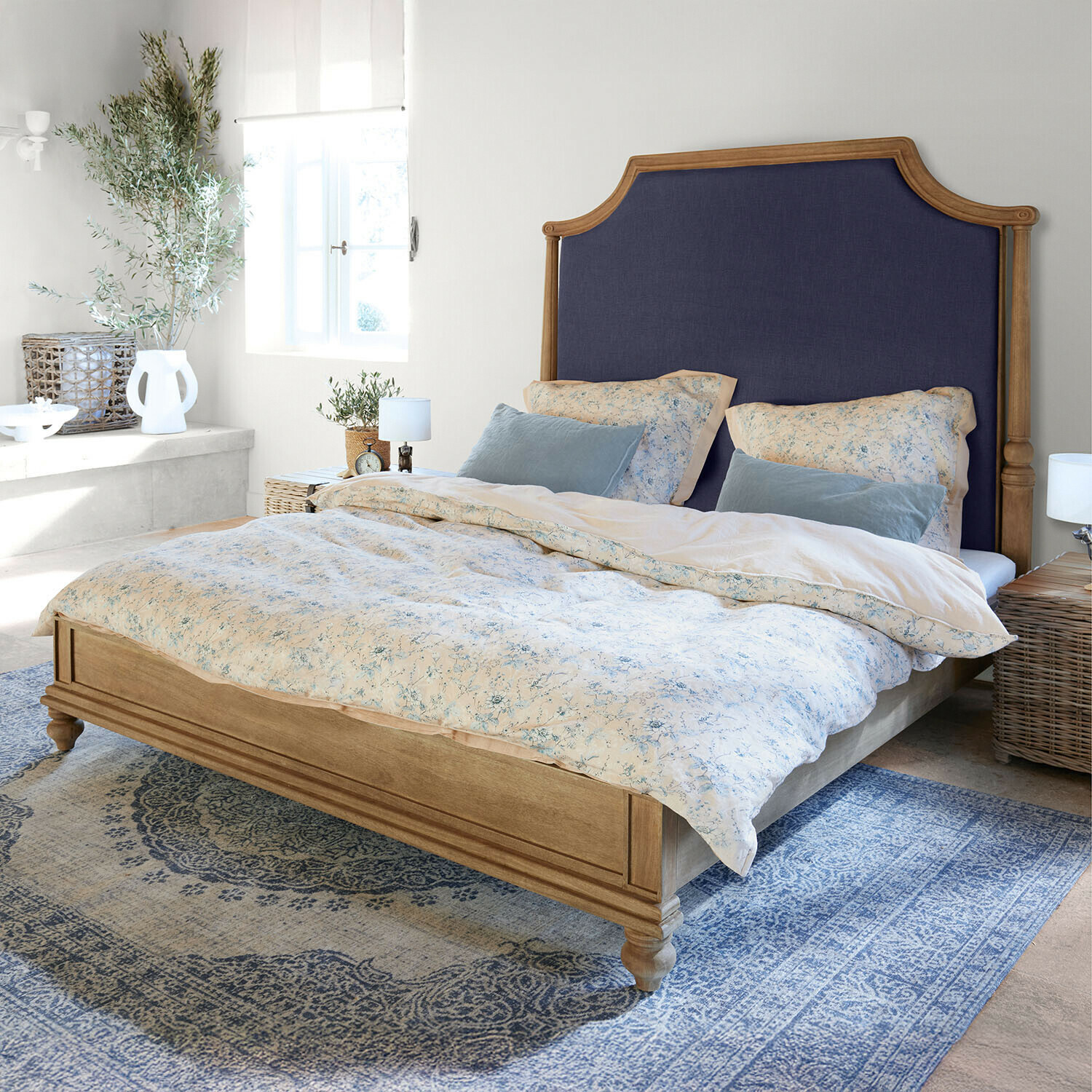 Holzbett mit dunkelblau gepolstertem Kopfteil in hellem Schlafzimmer mit blauem Teppich