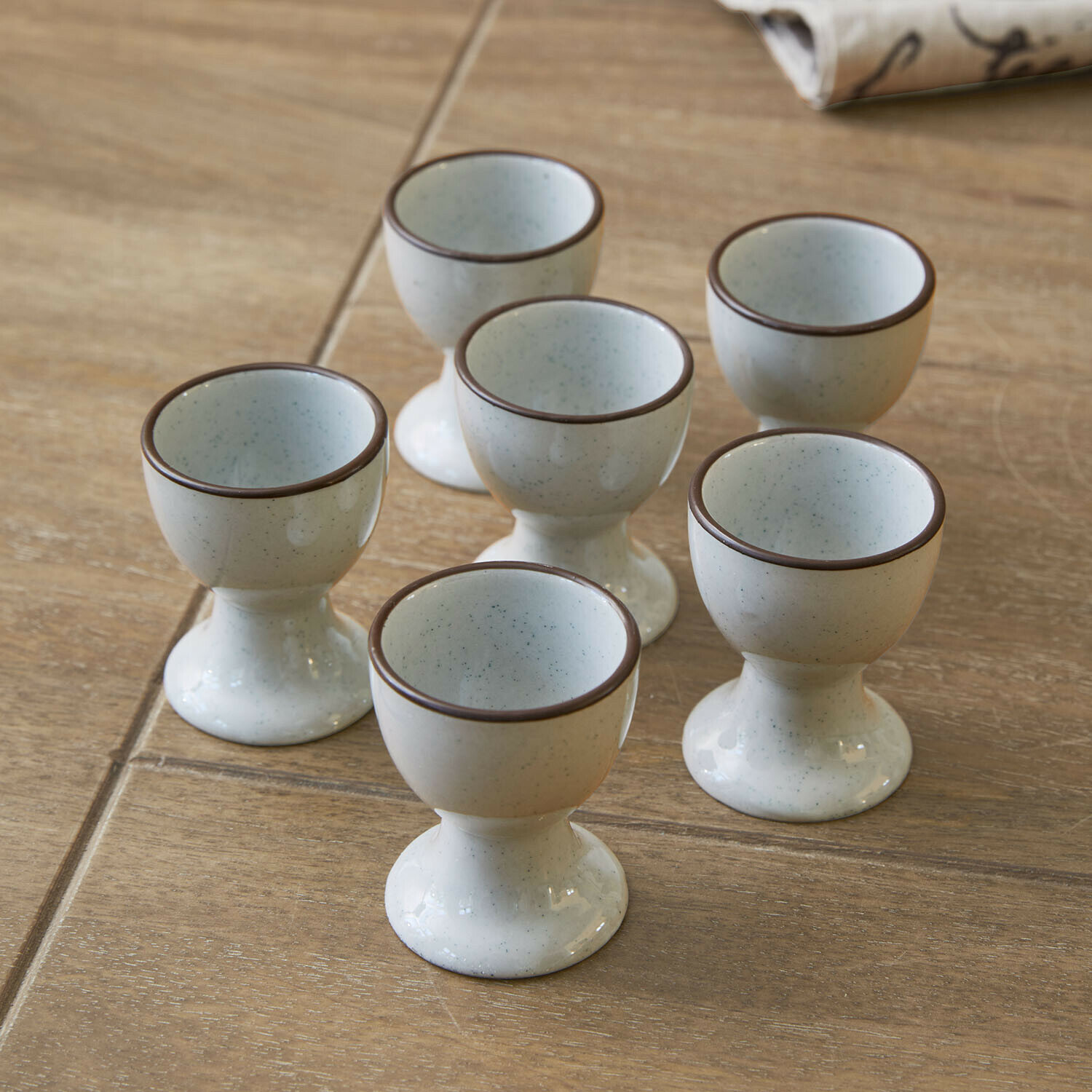 Eierbecher 6er Set Biarré Set mit sechs cremefarbenen Keramik-Eierbechern mit braunem Rand auf Holztisch