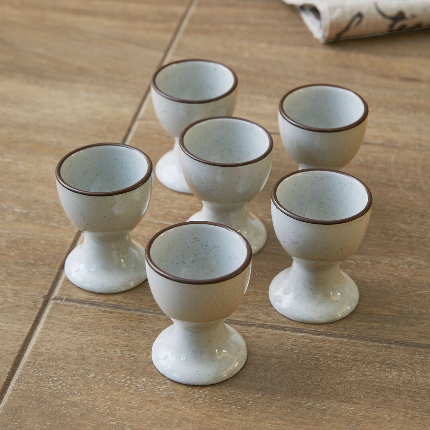 Eierbecher 6er Set Biarré Set mit sechs cremefarbenen Keramik-Eierbechern mit braunem Rand auf Holztisch