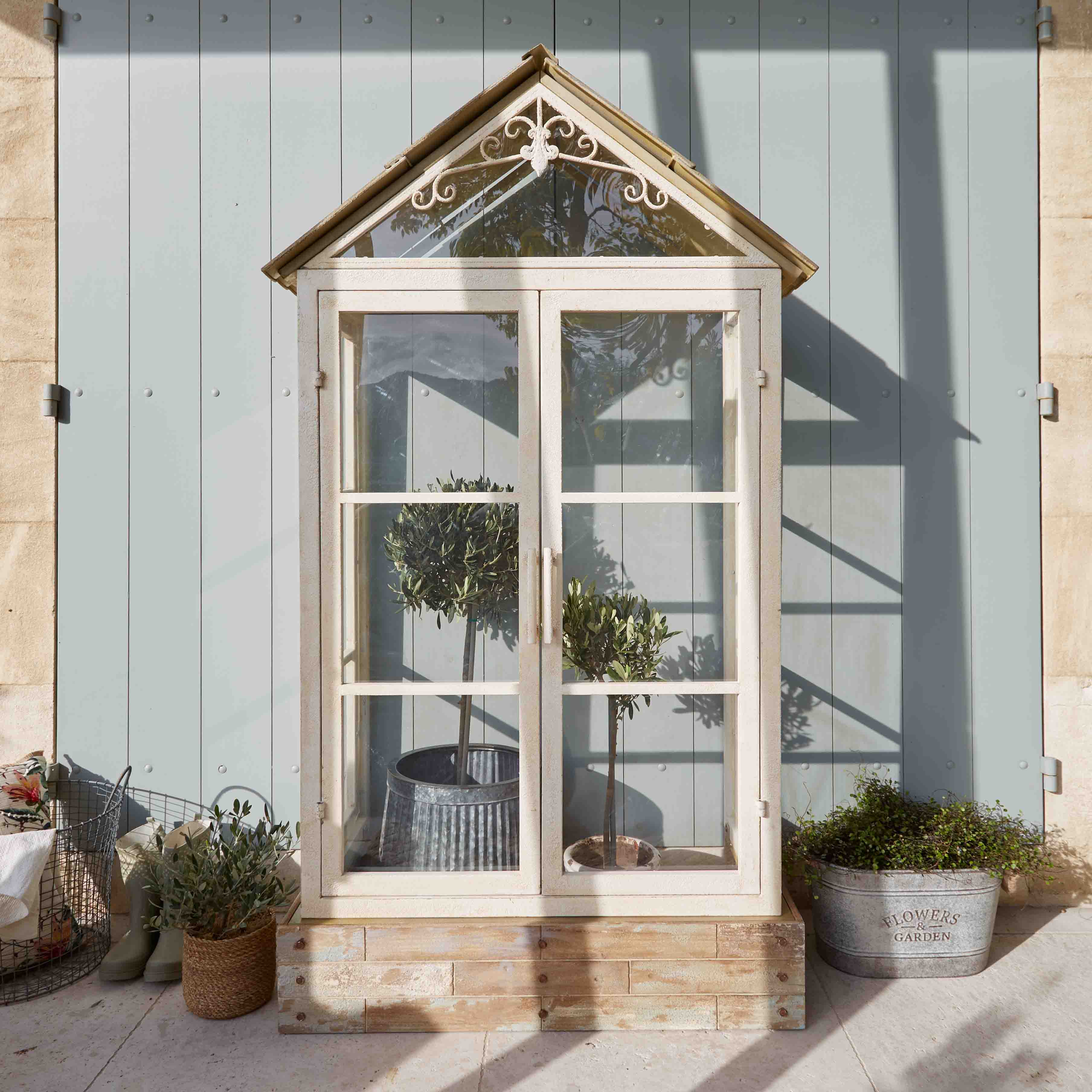 Weisses Holz-Gewächshaus mit dekorativem Dach und Pflanzen in Töpfen auf Terrasse