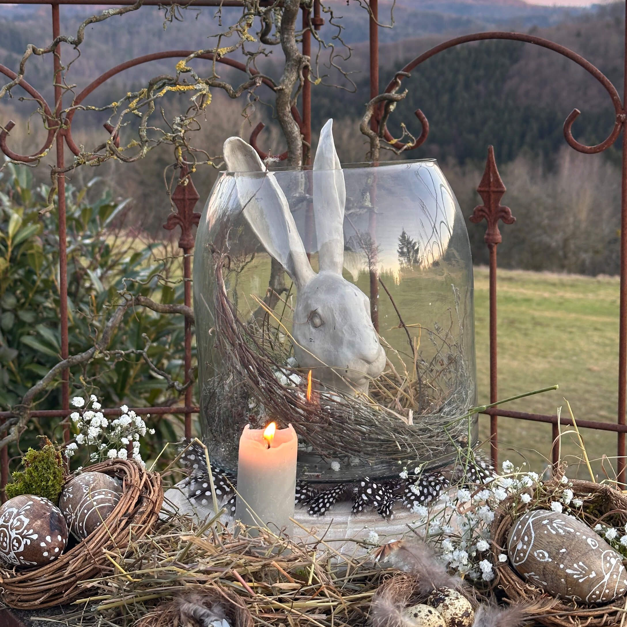 Natürlich dekorierte Osterfreude mit weissem Keramikhasen in Glasvase und brennender Kerze im rustikalen Stil