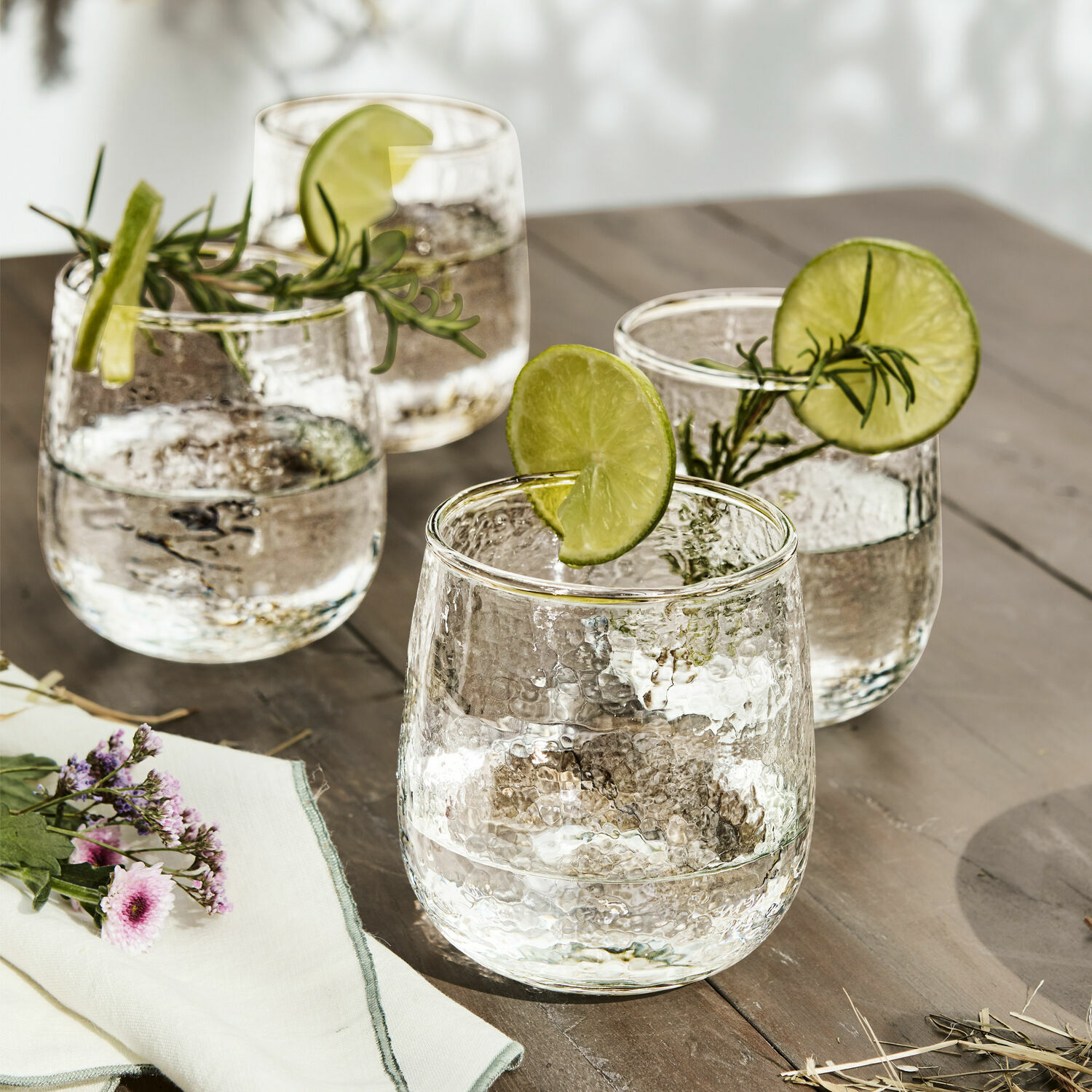 Glas 4er Set Valters Vier Gläser aus gehämmertem Glas mit Limettenscheiben und Rosmarinzweigen auf einem Holztisch
